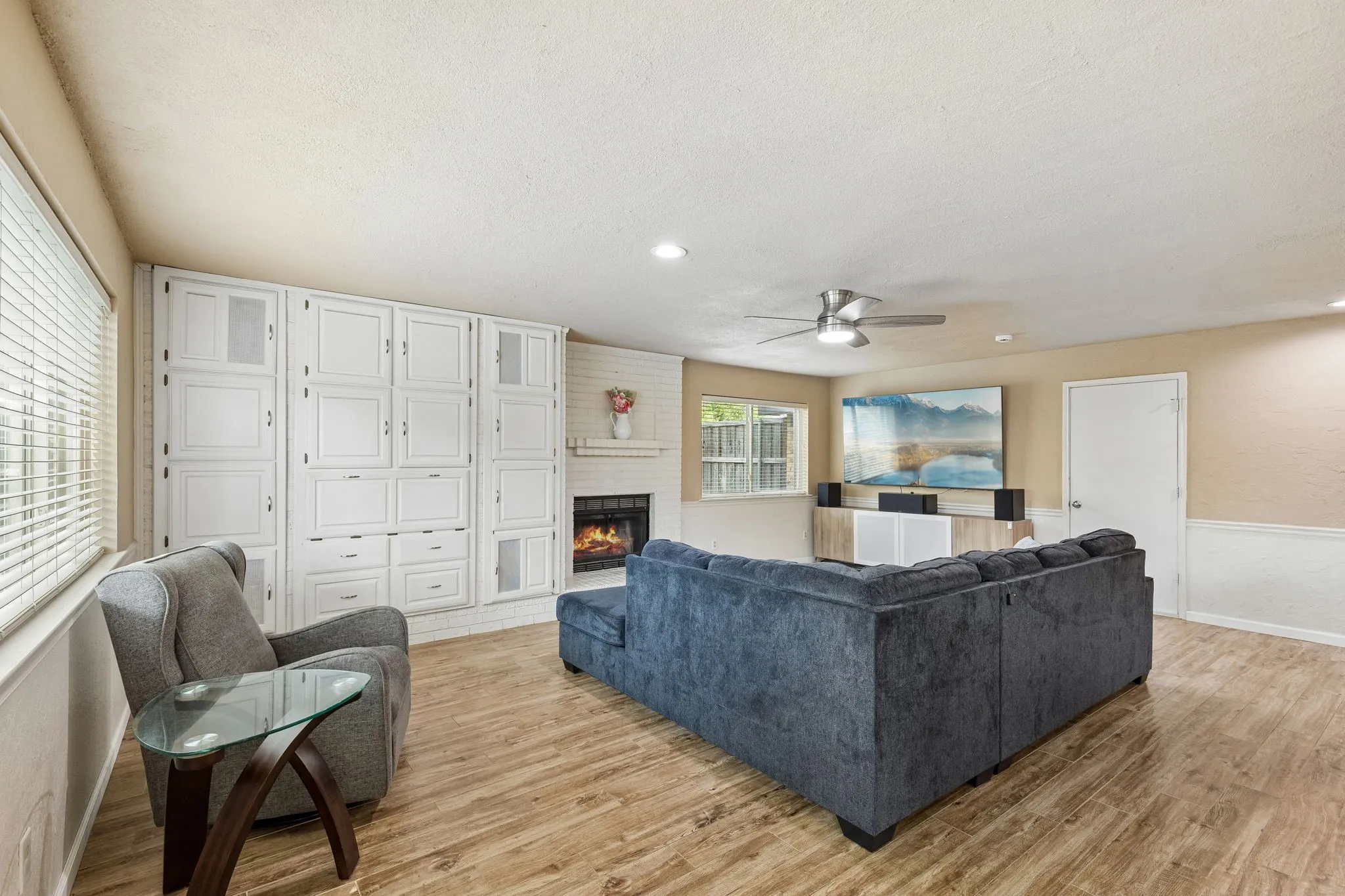 Living room with a brick fireplace, ceiling fan, light wood-style floors, a textured ceiling, and recessed lighting