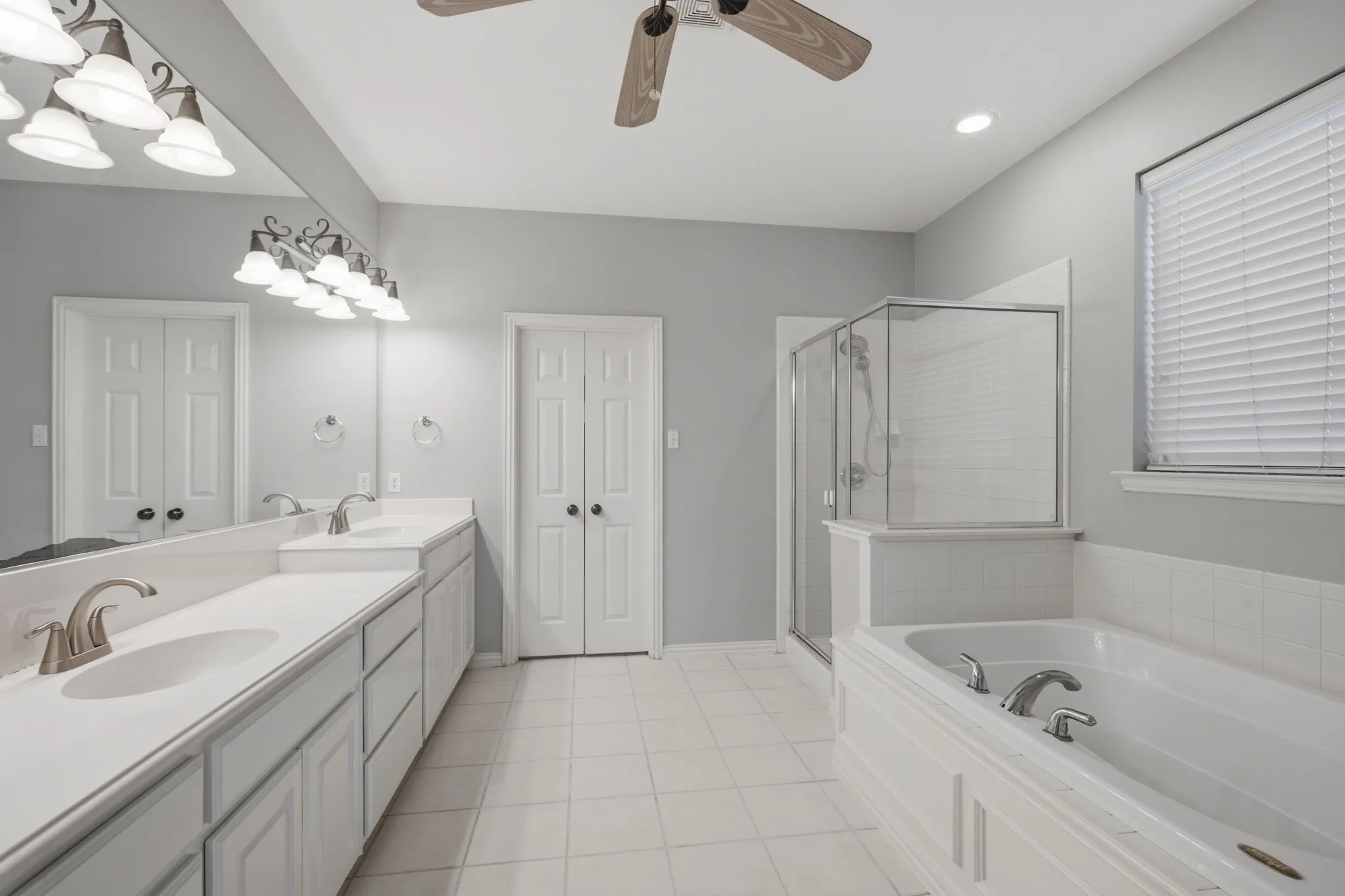 This spacious primary bathroom offers a retreat, featuring a garden soaking tub and a separate glass-enclosed shower. The room is completed by double doors that open into an expansive, oversized walk-in closet with plenty of storage space.