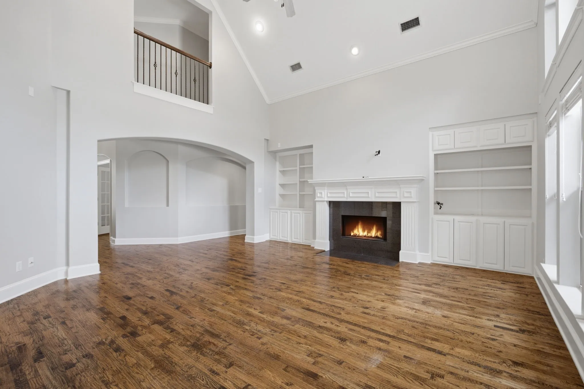 This spacious and inviting family room serves as the heart of the home, featuring an impressive vaulted ceiling that creates an open, airy atmosphere. A second-floor balcony overlooks the living area, adding an architectural touch, while detailed, high-quality crown molding spans the entire room to provide a custom, polished finish. A wide, beautifully crafted arched entryway provides a seamless transition from the entrance hall, perfectly blending style and functionality in this central gathering space.