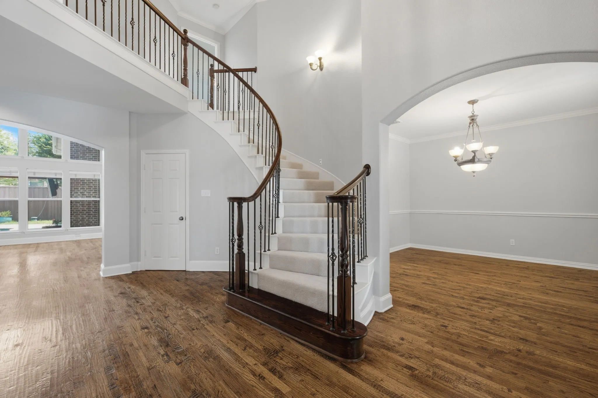 The photograph captures the stunning front of the structure, highlighting the grand entryway that showcases a magnificent spiral staircase complete with elegant, custom wrought iron railings. To the immediate right of the entrance, the spacious dining room is visible, providing a seamless flow and direct access into the gourmet kitchen area. Notice the solid hardwood floors that flow throughout.