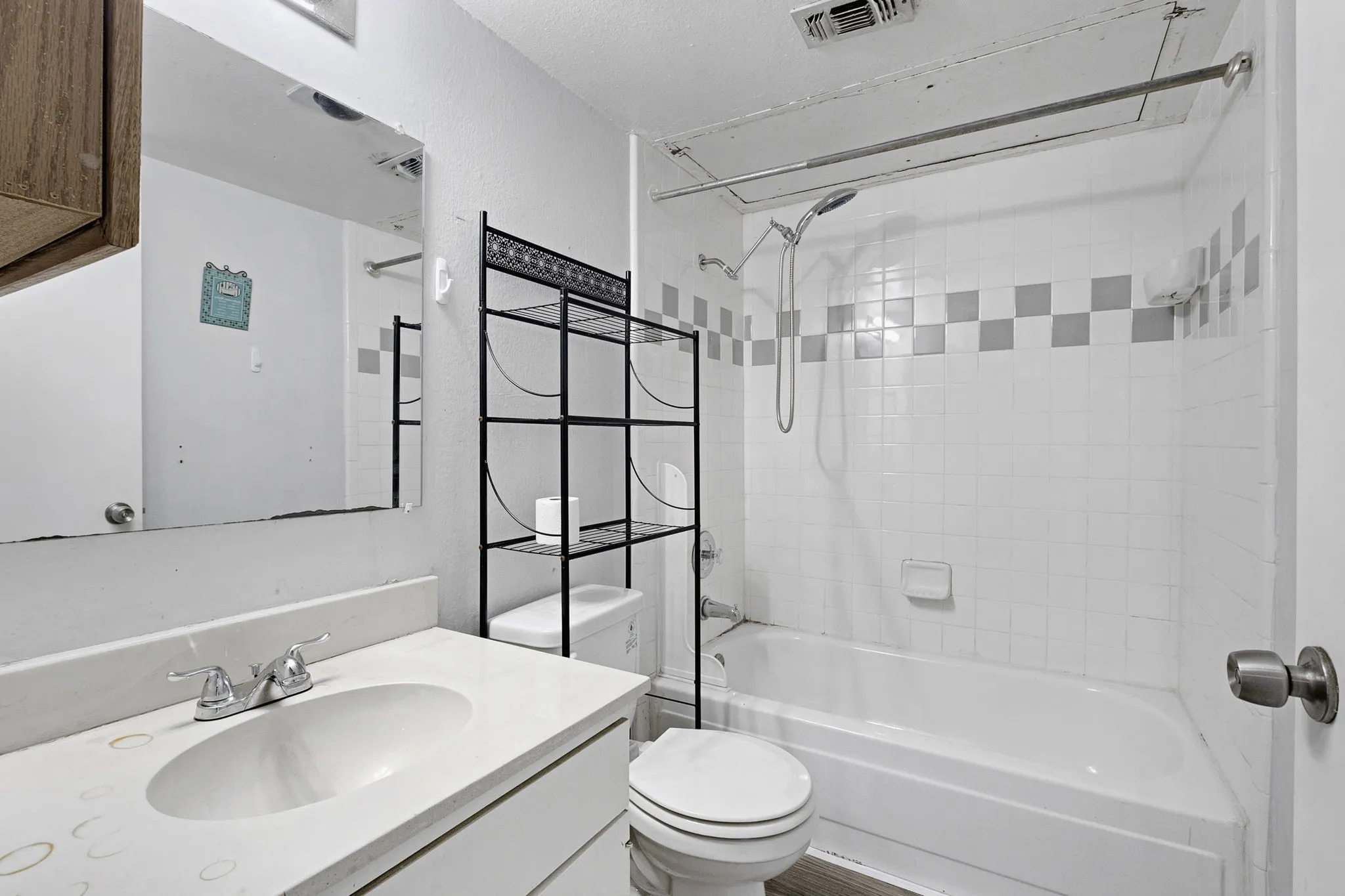 White tiled bathroom featuring a shower-tub combination with a checkered tile accent band