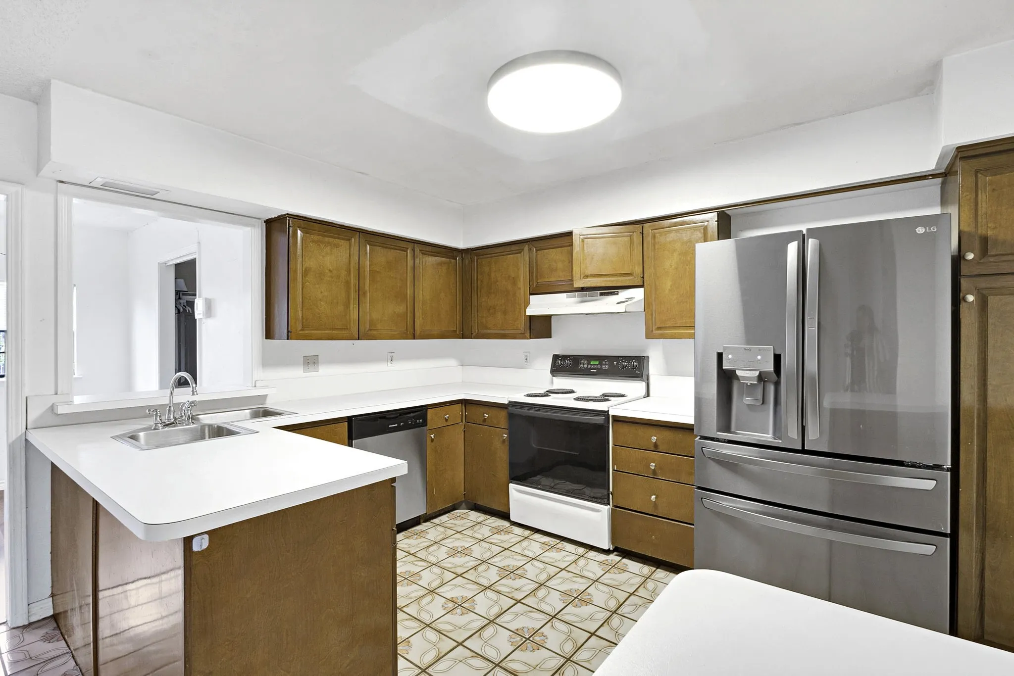 Kitchen featuring wood cabinetry, white countertops, stainless steel refrigerator, white electric range, and tile flooring