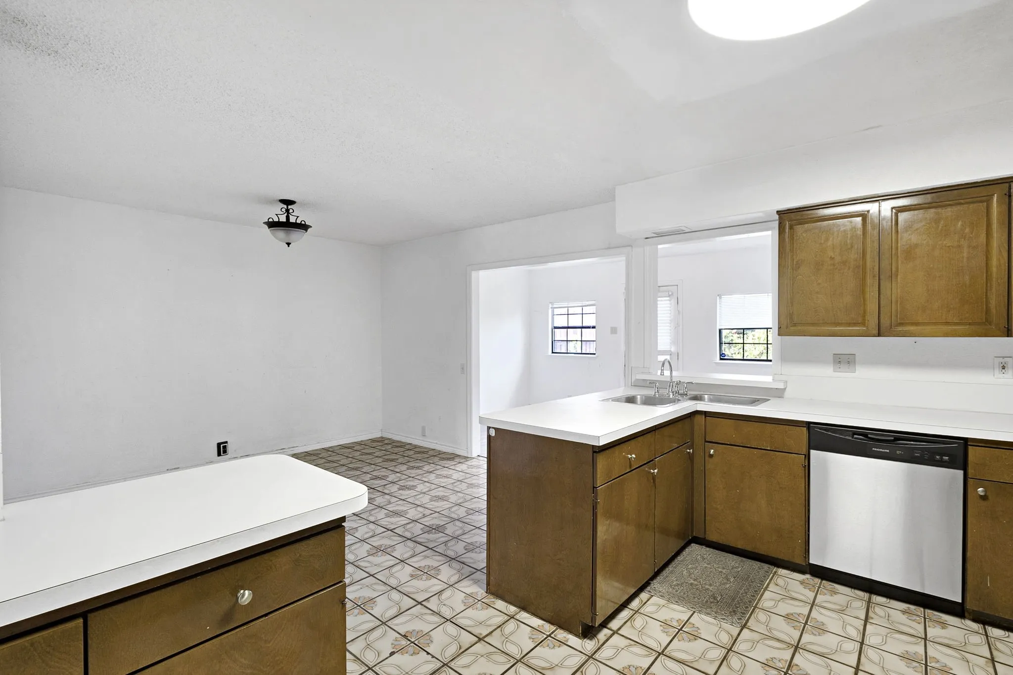 Kitchen featuring wood-finish cabinetry, white countertops, a stainless steel dishwasher, and a double basin sink with a window overhead