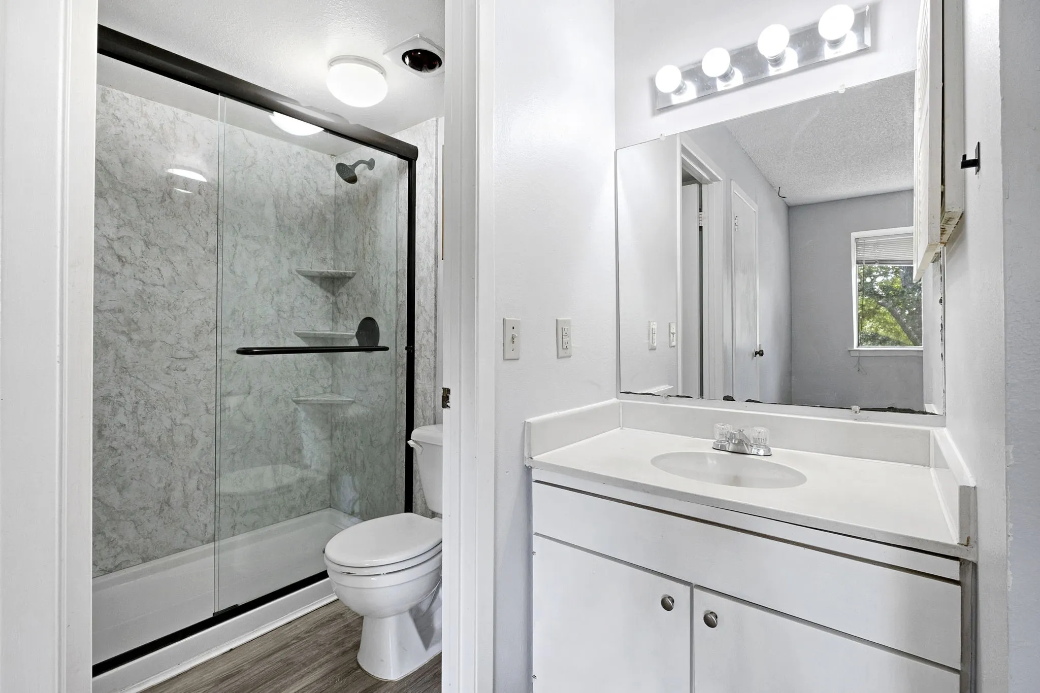 Bathroom featuring a white vanity with an integrated sink, a large mirror, and a four-bulb vanity light fixture