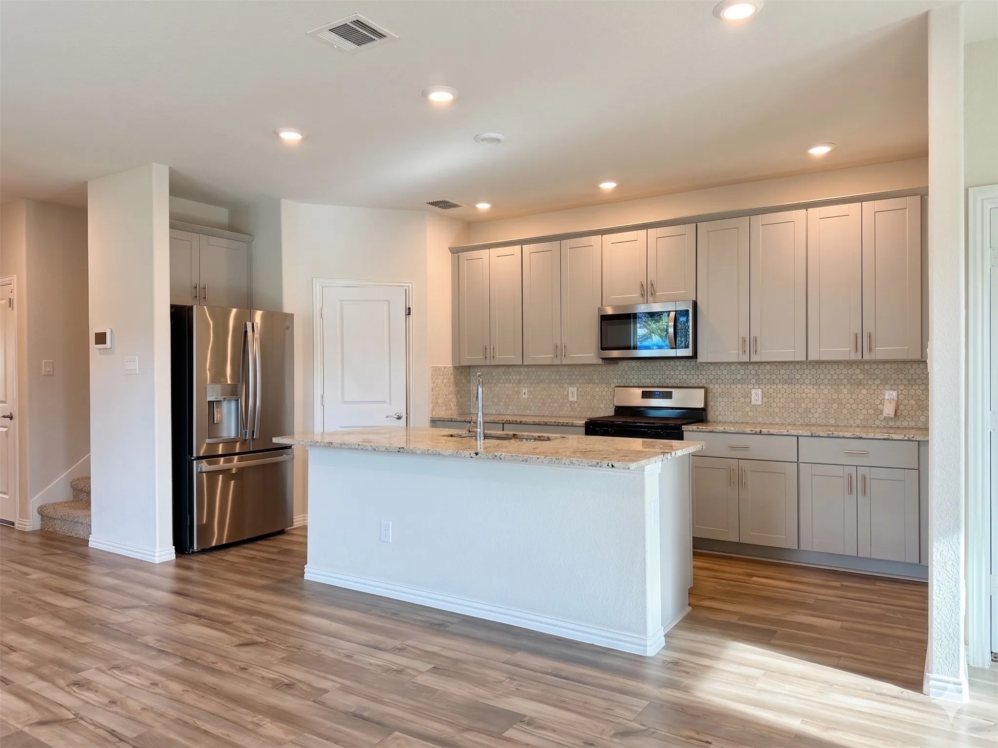 Kitchen featuring light gray cabinetry, stainless steel appliances, a center island with a sink, patterned backsplash, and recessed lighting