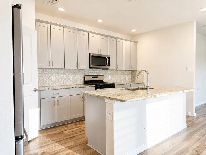 Modern kitchen featuring light gray shaker cabinetry, a patterned tile backsplash, stainless steel appliances, and wood-finish flooring