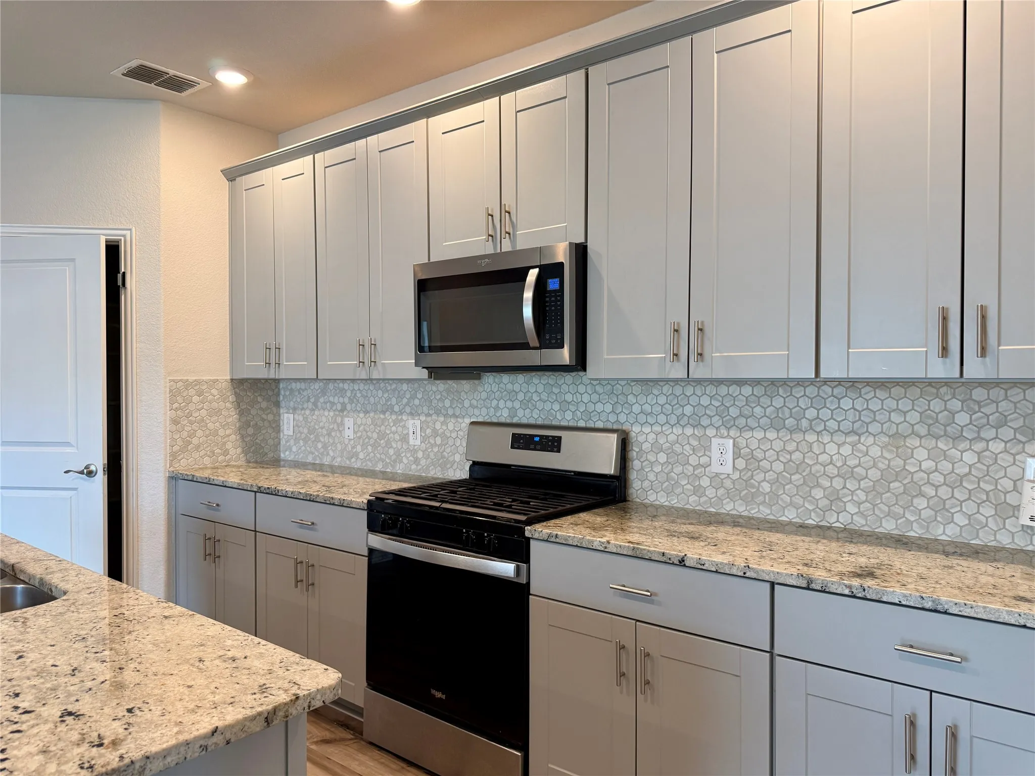 Kitchen featuring extensive light gray cabinetry, speckled countertops, and a white hexagonal tile backsplash