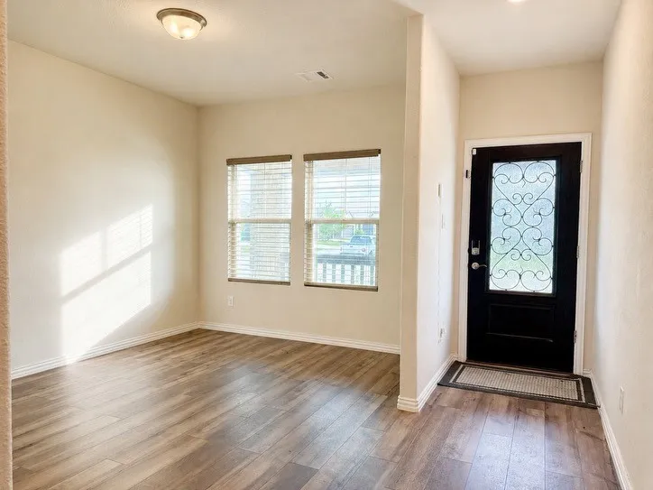 Entryway featuring a decorative glass-paneled front door, wood-finish flooring, and two windows with blinds