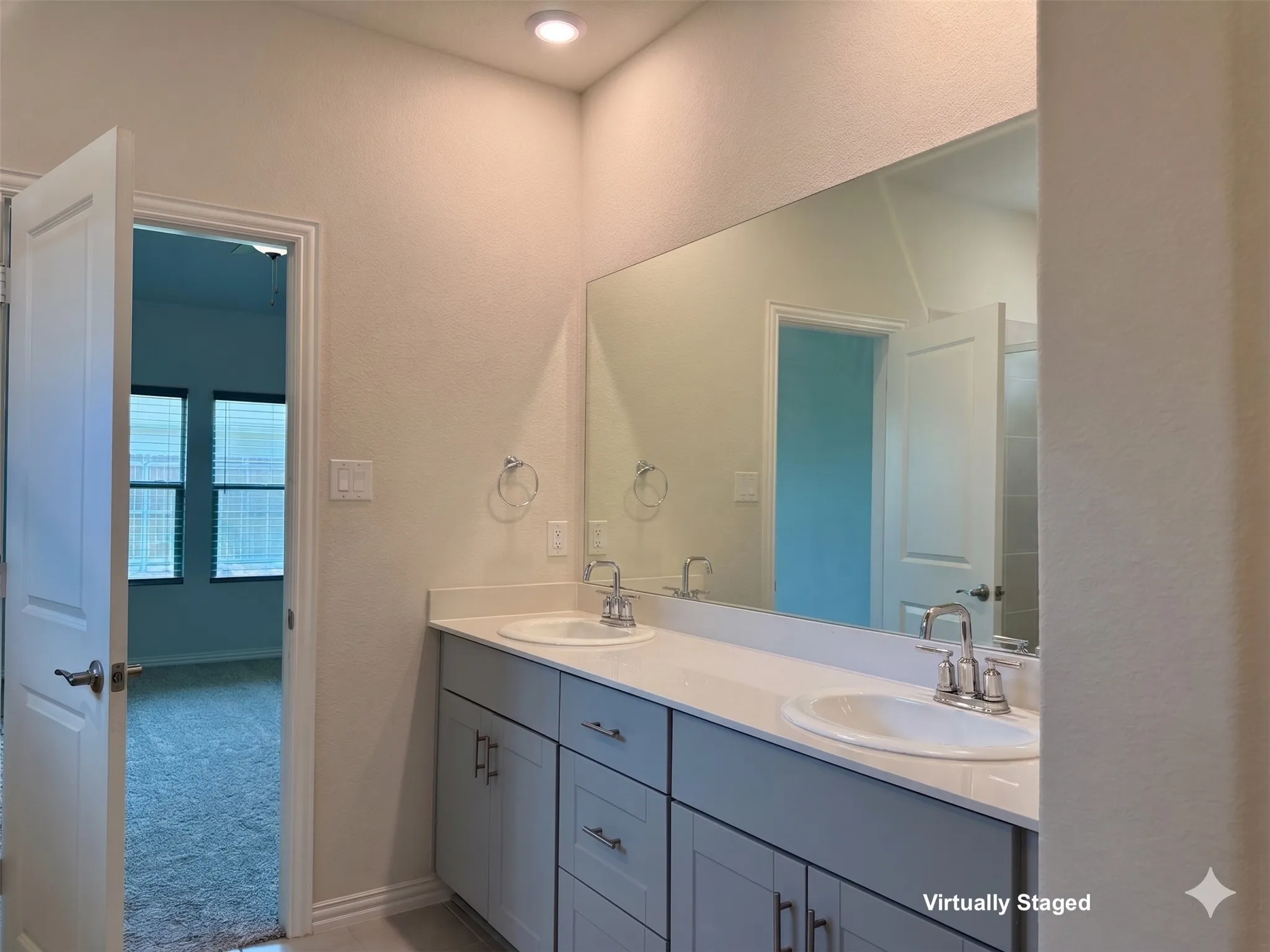 Dual vanity with light gray cabinetry and white countertops, featuring chrome fixtures and an expansive wall-mounted mirror
