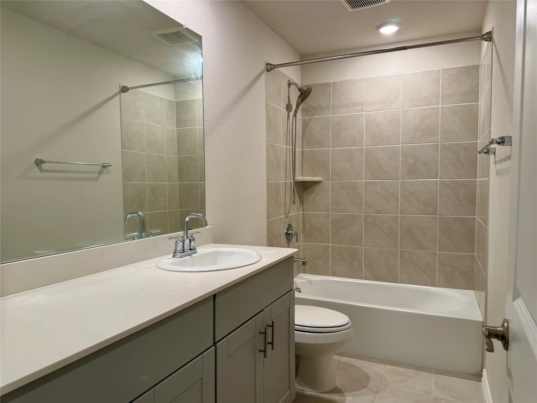 Bathroom featuring a vanity with an integrated sink and chrome fixtures, a tiled shower/tub combination with a built-in shelf, and recessed lighting