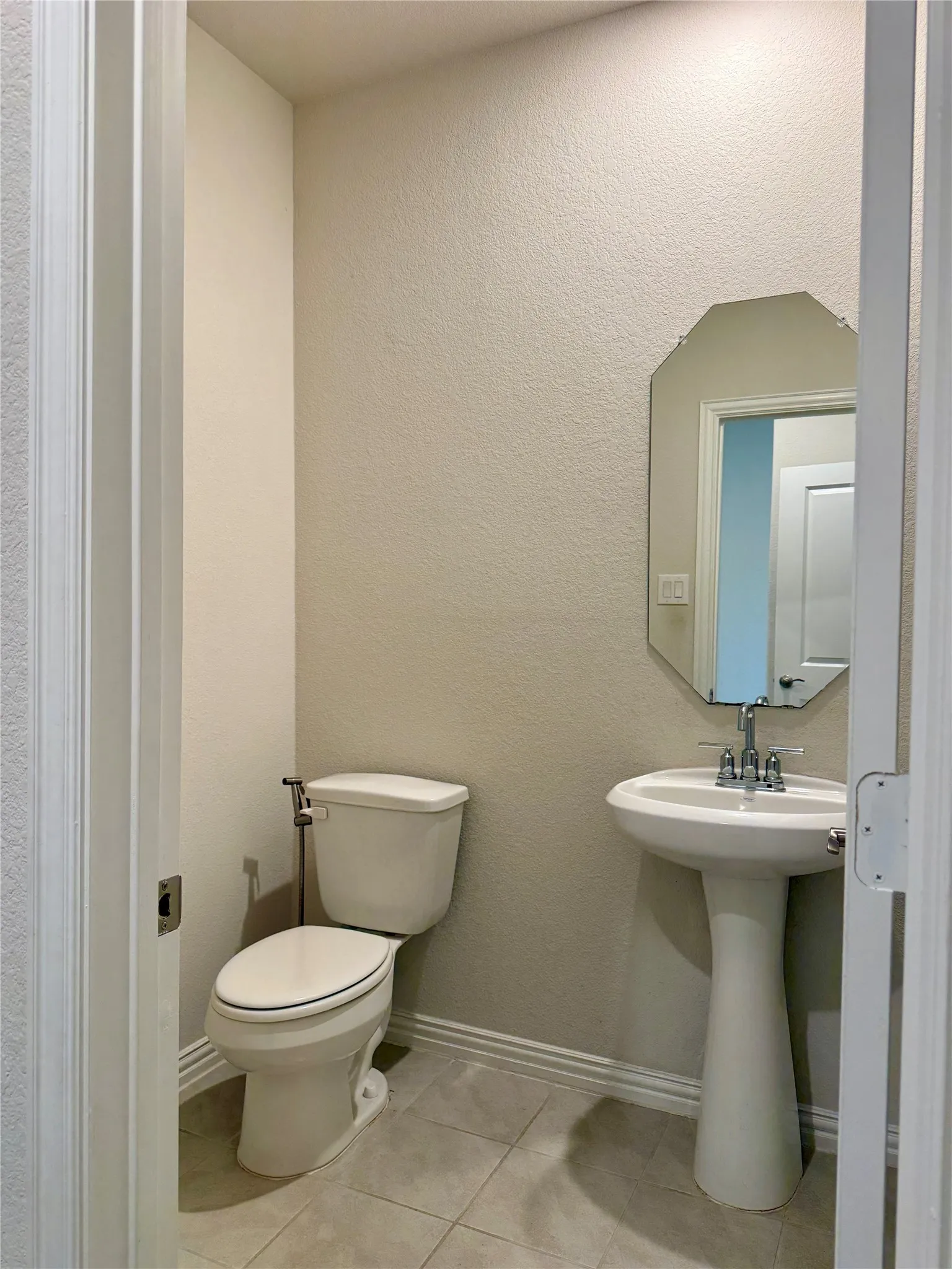 Pedestal sink with chrome faucet, complemented by a decorative octagonal mirror