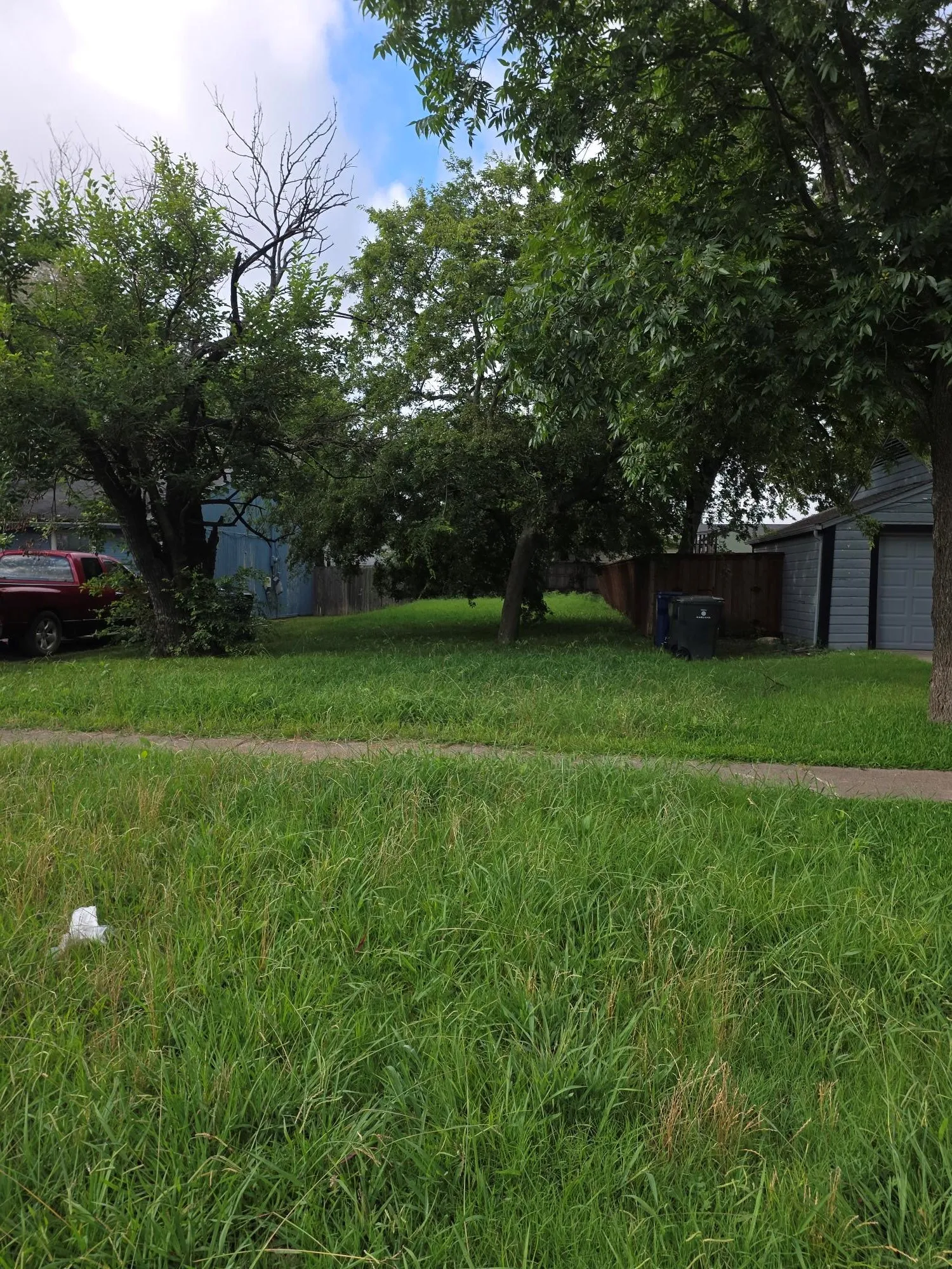 Expansive green lot featuring mature trees and a partial wood fence