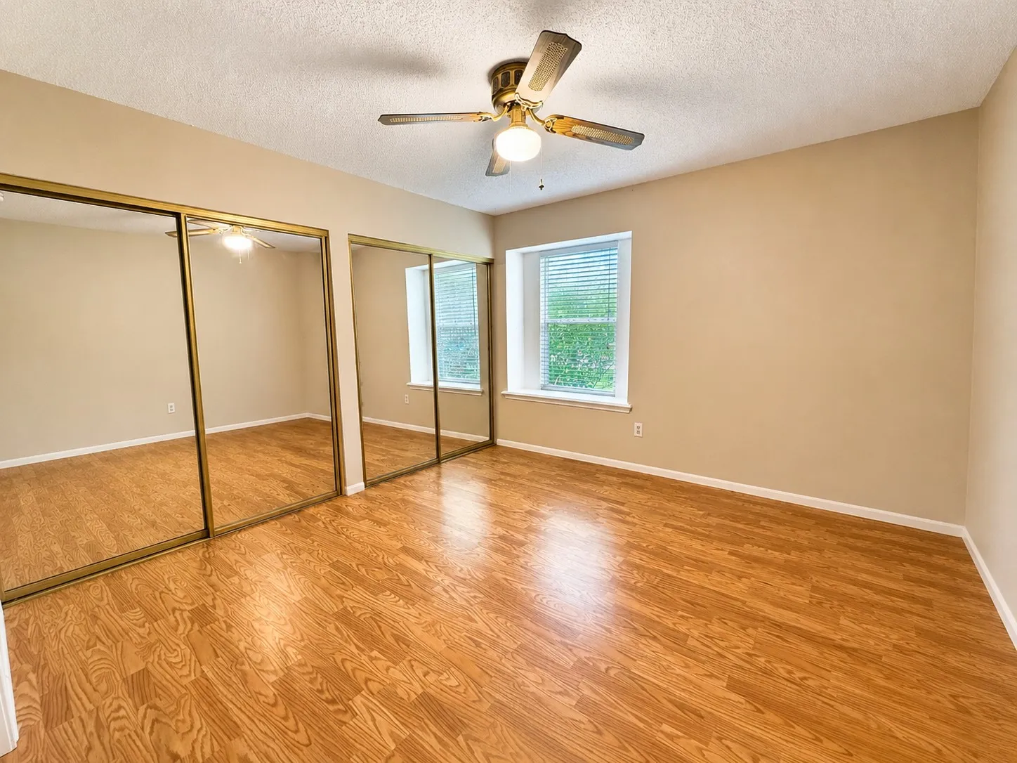 Room featuring wood-finish flooring, two windows with horizontal blinds, and a ceiling fan with light fixture