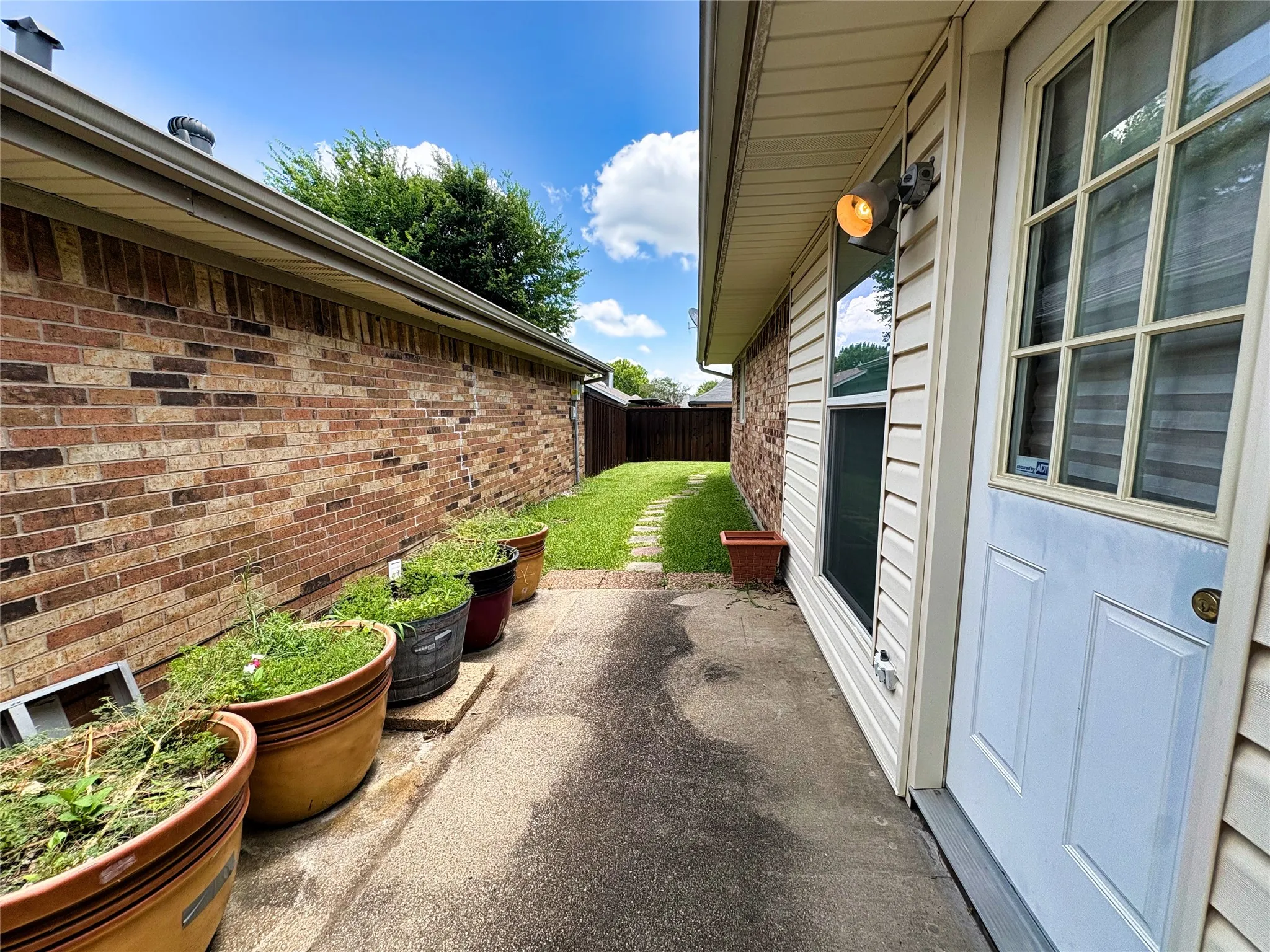 Exterior side passage featuring a brick wall, concrete walkway, vinyl siding, and a white paneled door with glass inserts