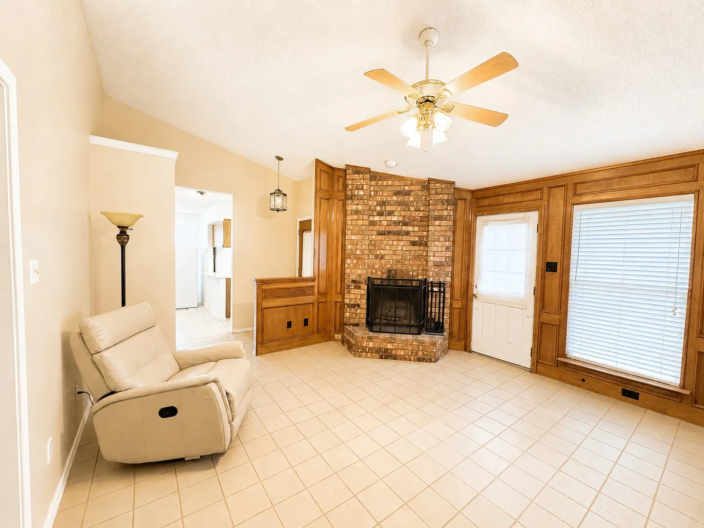 Living area featuring a brick fireplace with a black metal screen, wood-paneled walls, and light-toned square tile flooring