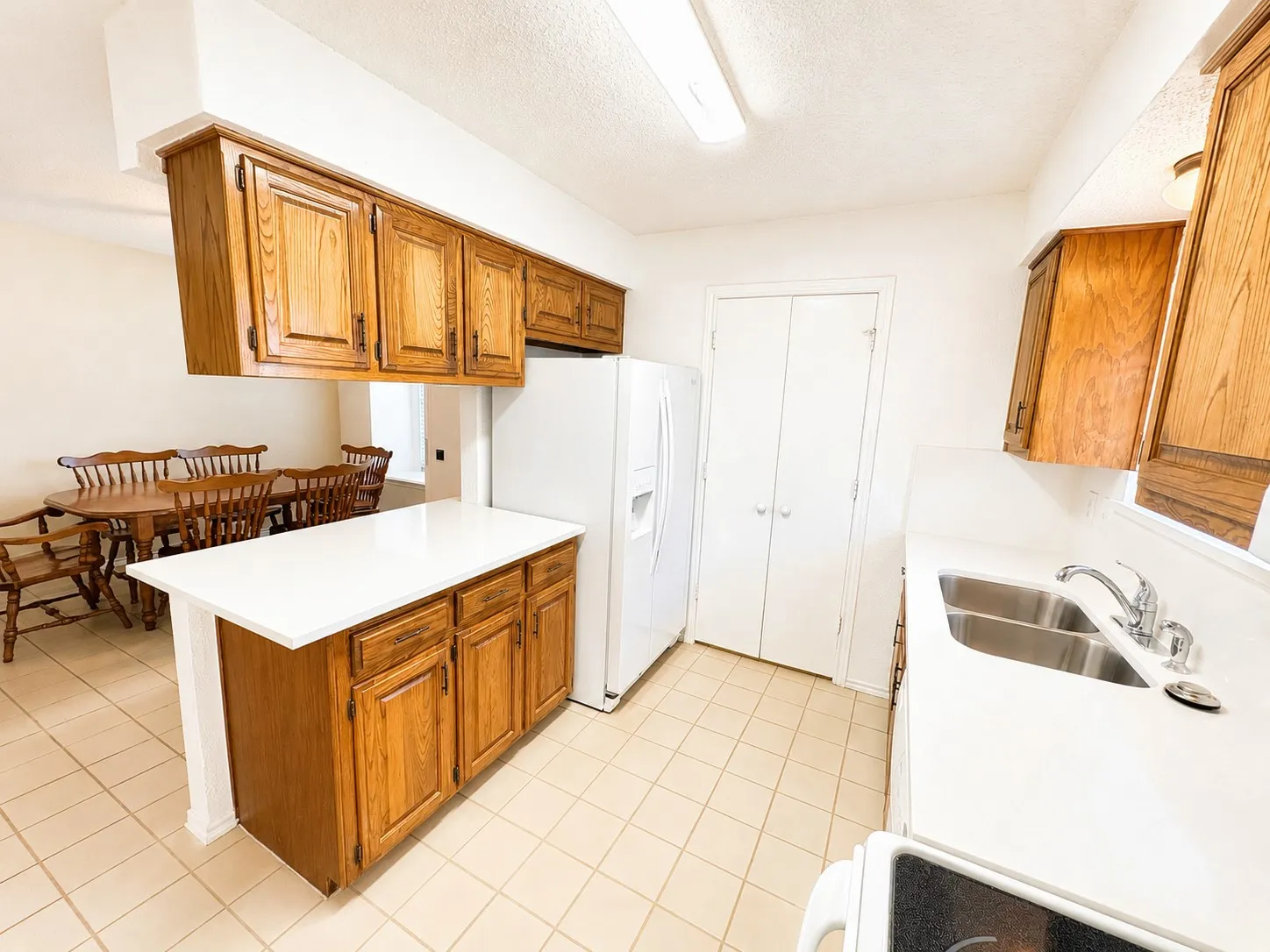 Kitchen featuring light wood cabinetry, white countertops, tile flooring, and a double basin stainless steel sink