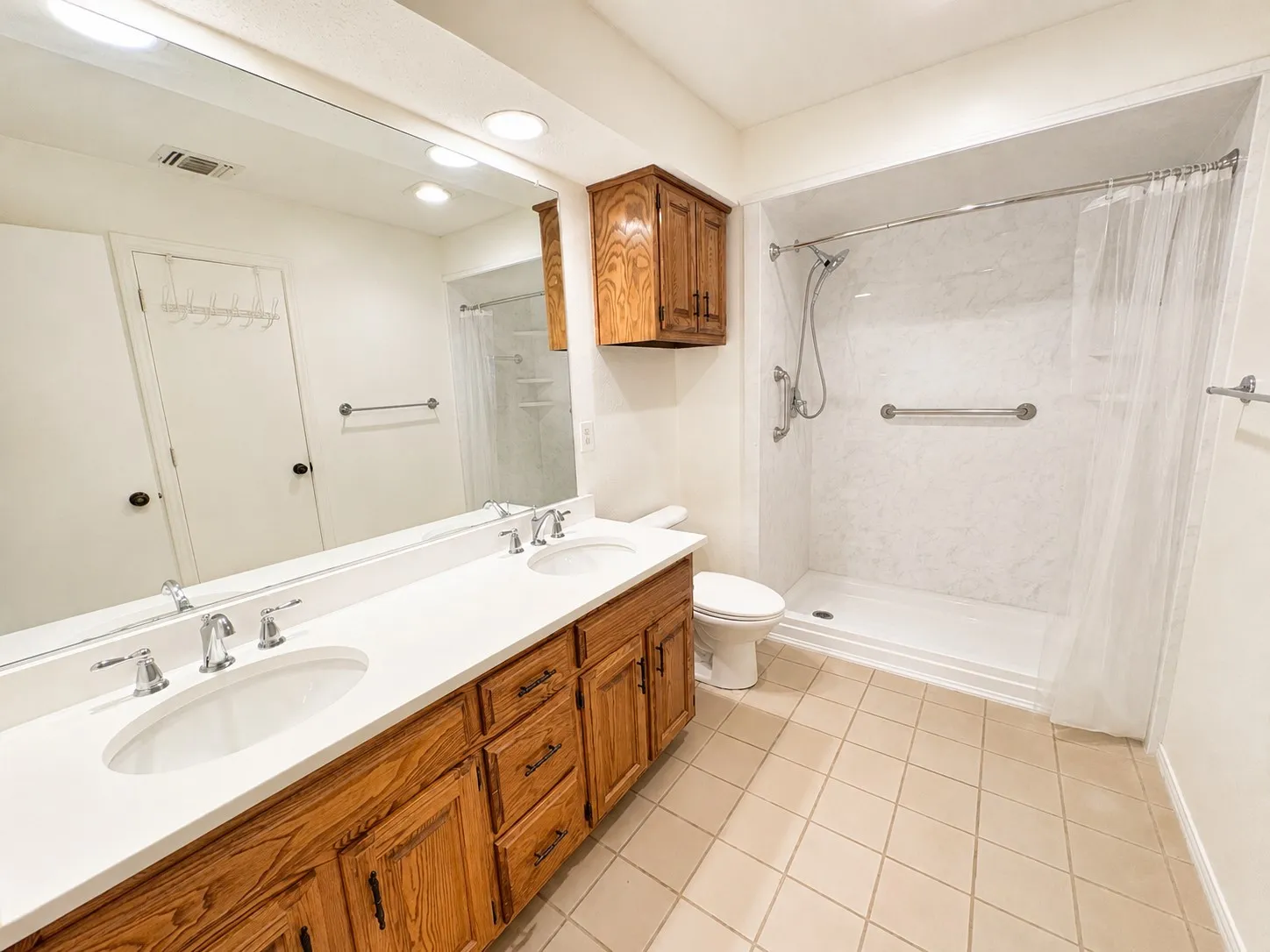 Bathroom featuring a dual vanity with white countertops, wood cabinetry, chrome fixtures, and an expansive mirror