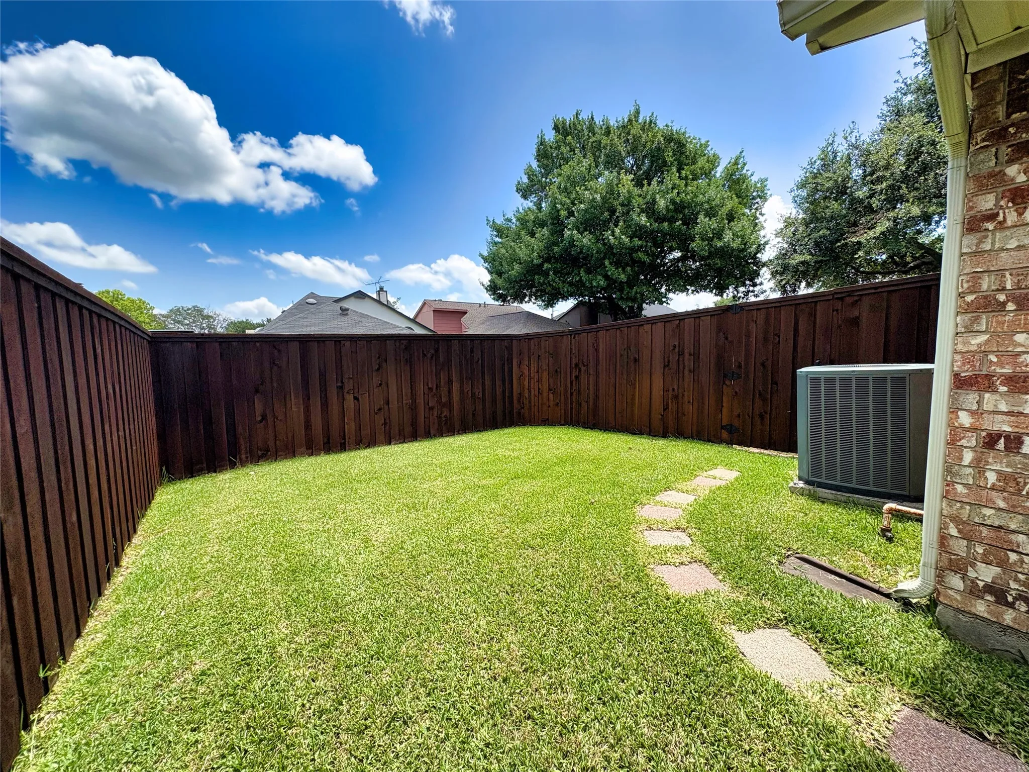 Private backyard featuring a dark-stained wood fence, natural grass lawn, and a stone paver pathway