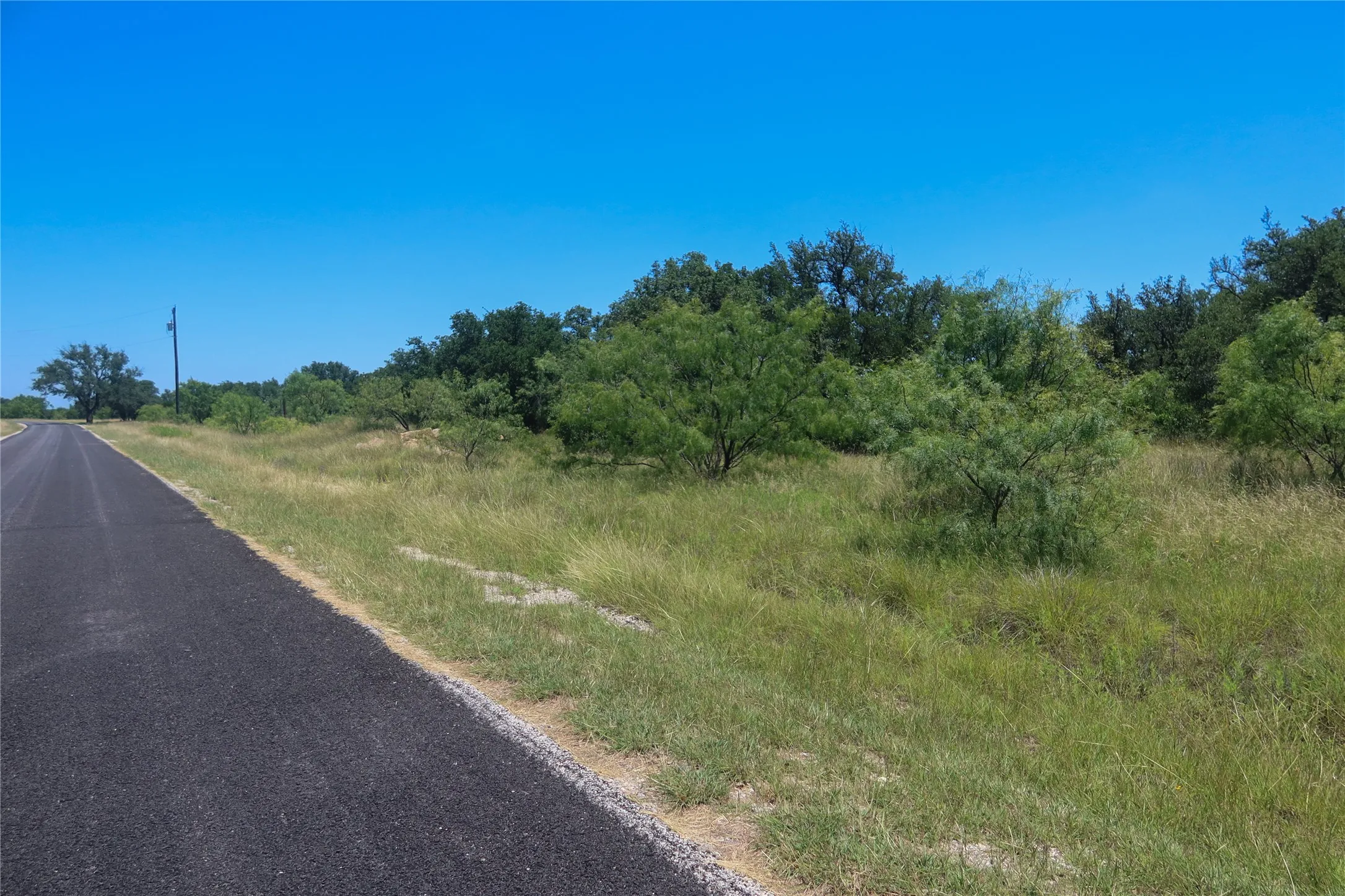 Paved road frontage bordering an expansive parcel of undeveloped land
