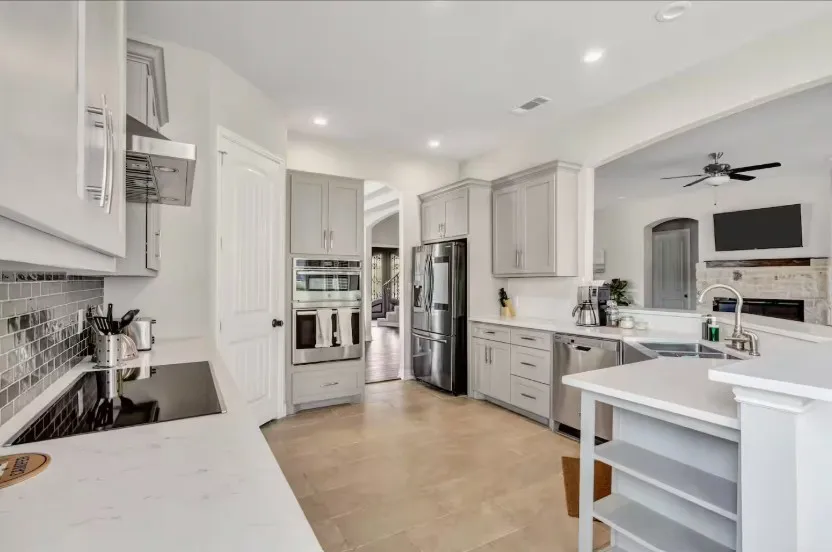 Contemporary kitchen featuring light gray cabinetry, stainless steel appliances, white quartz countertops, a mosaic tile backsplash, and light tile flooring