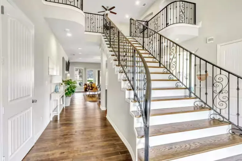Grand curved staircase with decorative wrought iron balusters and wood-finish treads
