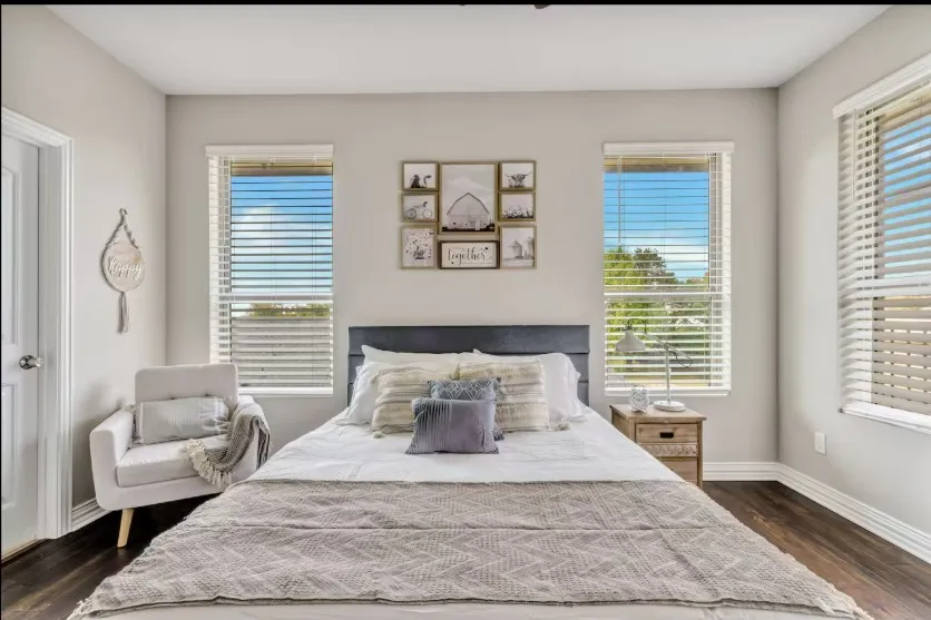 Bedroom featuring two windows with white blinds, dark wood-finish flooring, and white baseboards