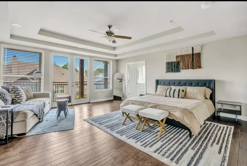 Spacious room featuring wood-finish flooring, a tray ceiling with recessed lighting and a ceiling fan, and double French doors opening to a balcony