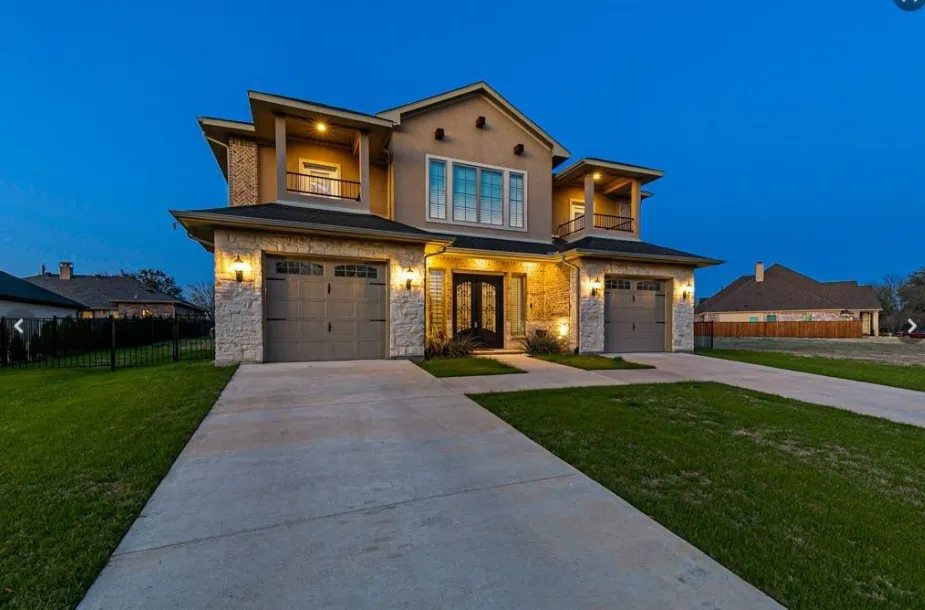 Modern stucco and stone facade featuring a dual garage, double-door entry, and two upper balconies