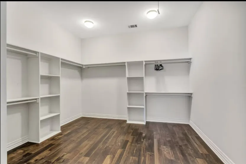 Spacious closet featuring custom built-in shelving and hanging rods