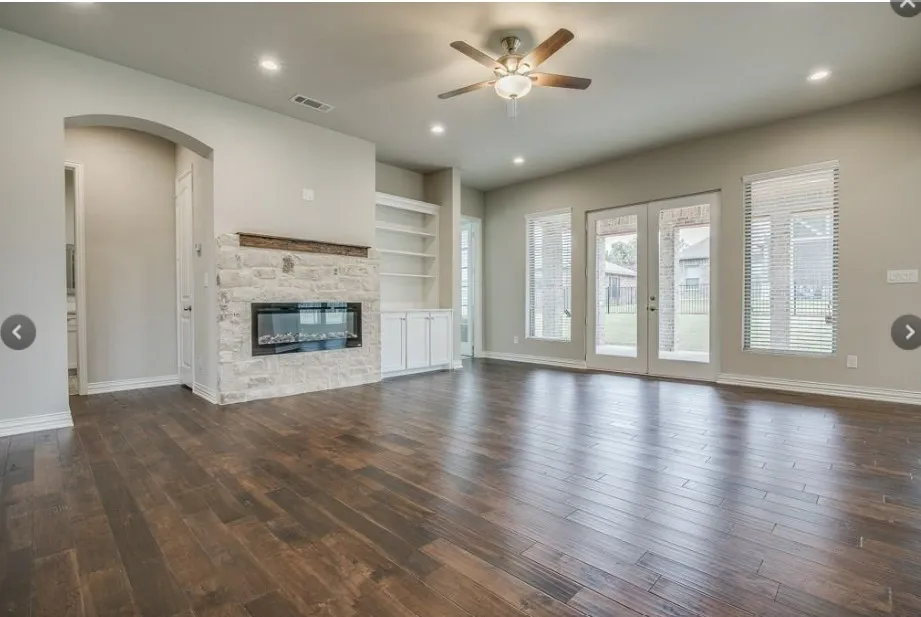 Spacious interior featuring wood-finish flooring, a stone fireplace with a wood mantle, built-in shelving and cabinetry, recessed lighting, and a ceiling fan