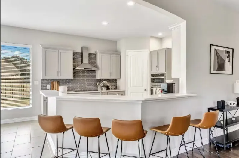 Open-concept kitchen featuring light-toned cabinetry, stainless steel appliances, a tiled backsplash, recessed lighting, and a breakfast bar with a white countertop