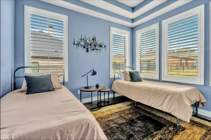 Room featuring three large windows with white louvered shutters, a tray ceiling, and light blue walls