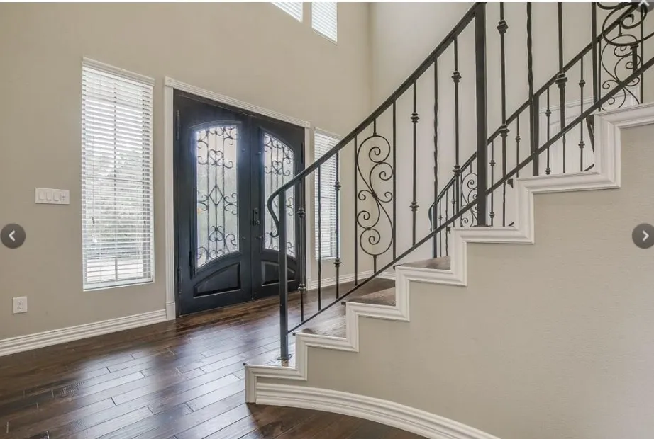 Grand entry foyer featuring an ornate double door, rich wood-finish flooring, and a curved staircase with wrought iron balusters