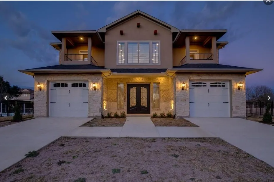 Stucco and stone facade featuring a two-car garage with carriage-style doors, an arched entry, and a prominent second-story balcony