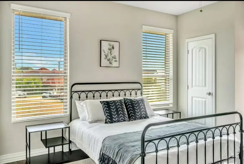 Spacious room featuring light gray walls, dark wood-finish flooring, and two tall windows with horizontal blinds