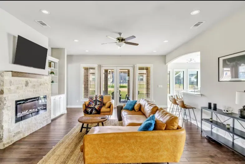 Spacious living area featuring wood-finish flooring, a stone-accented fireplace with a wood mantle, and built-in shelving