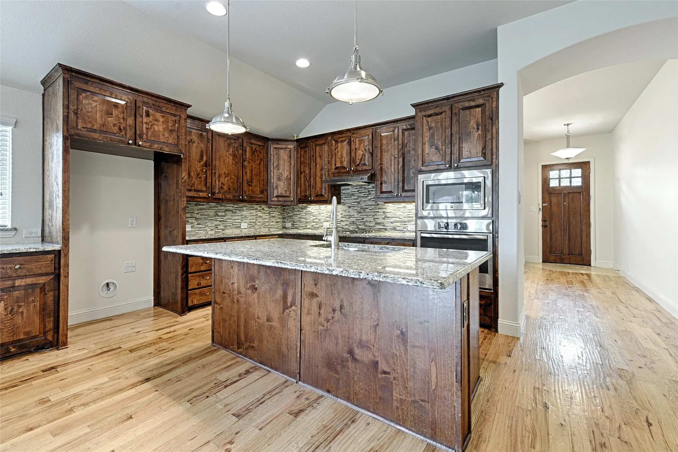 Kitchen featuring rich wood cabinetry, granite countertops, stainless steel appliances, a tiled backsplash, and wood-finish flooring