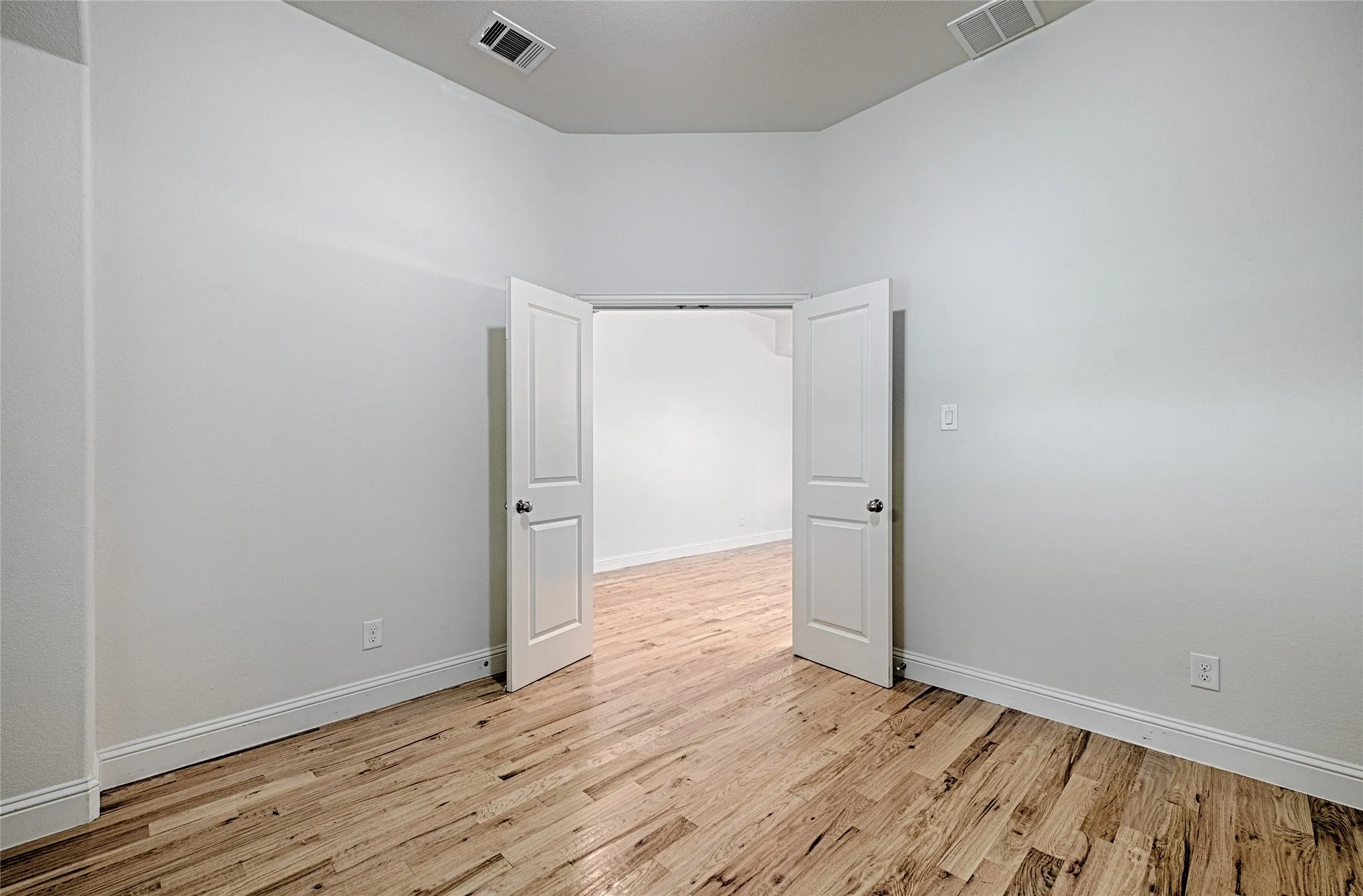 Room featuring wood-finish flooring, crisp white walls, white trim, and double panel doors