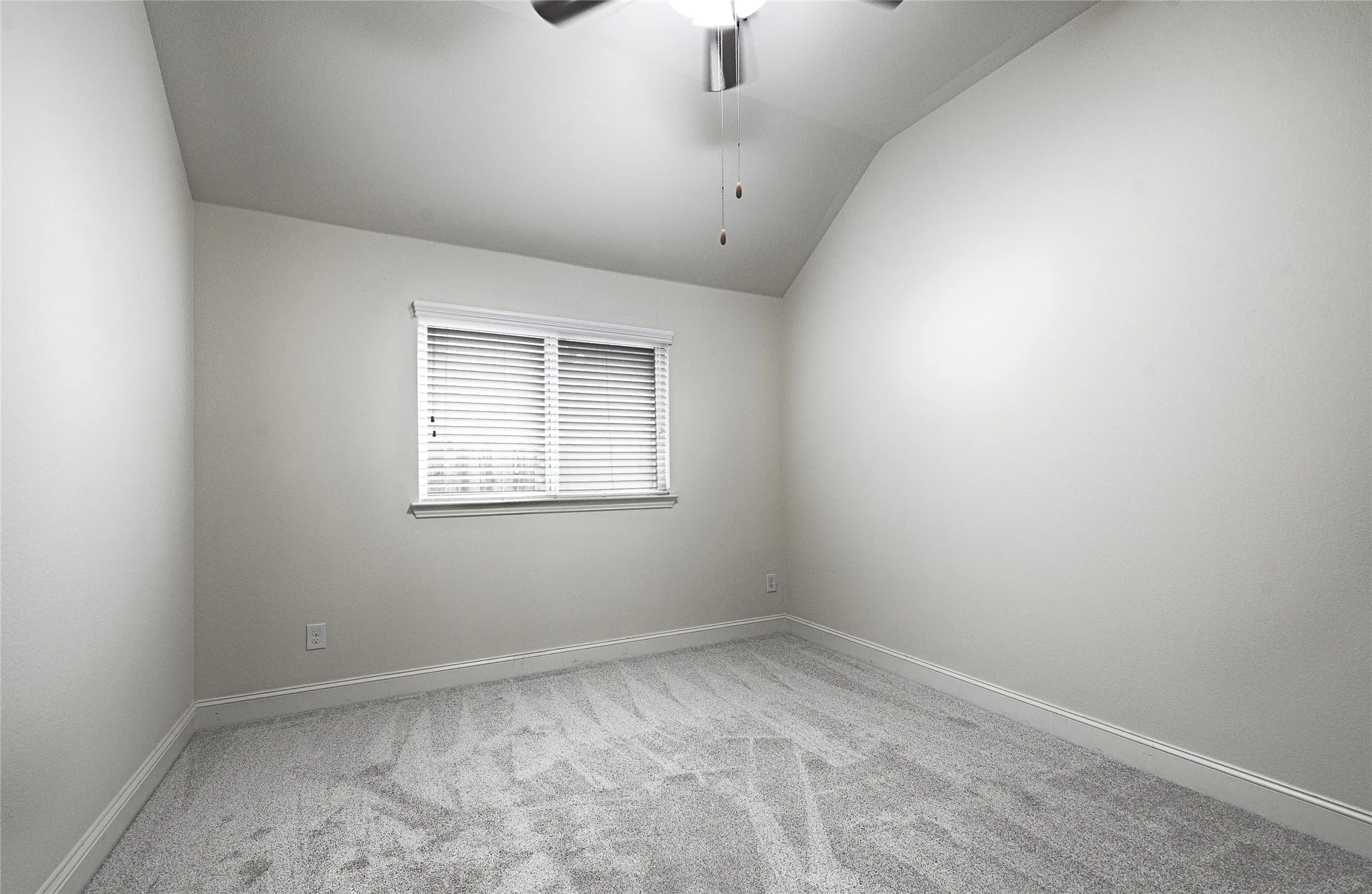 Bright room featuring sloped ceilings, a window with horizontal blinds, gray textured carpeting, and a ceiling fan with integrated lighting