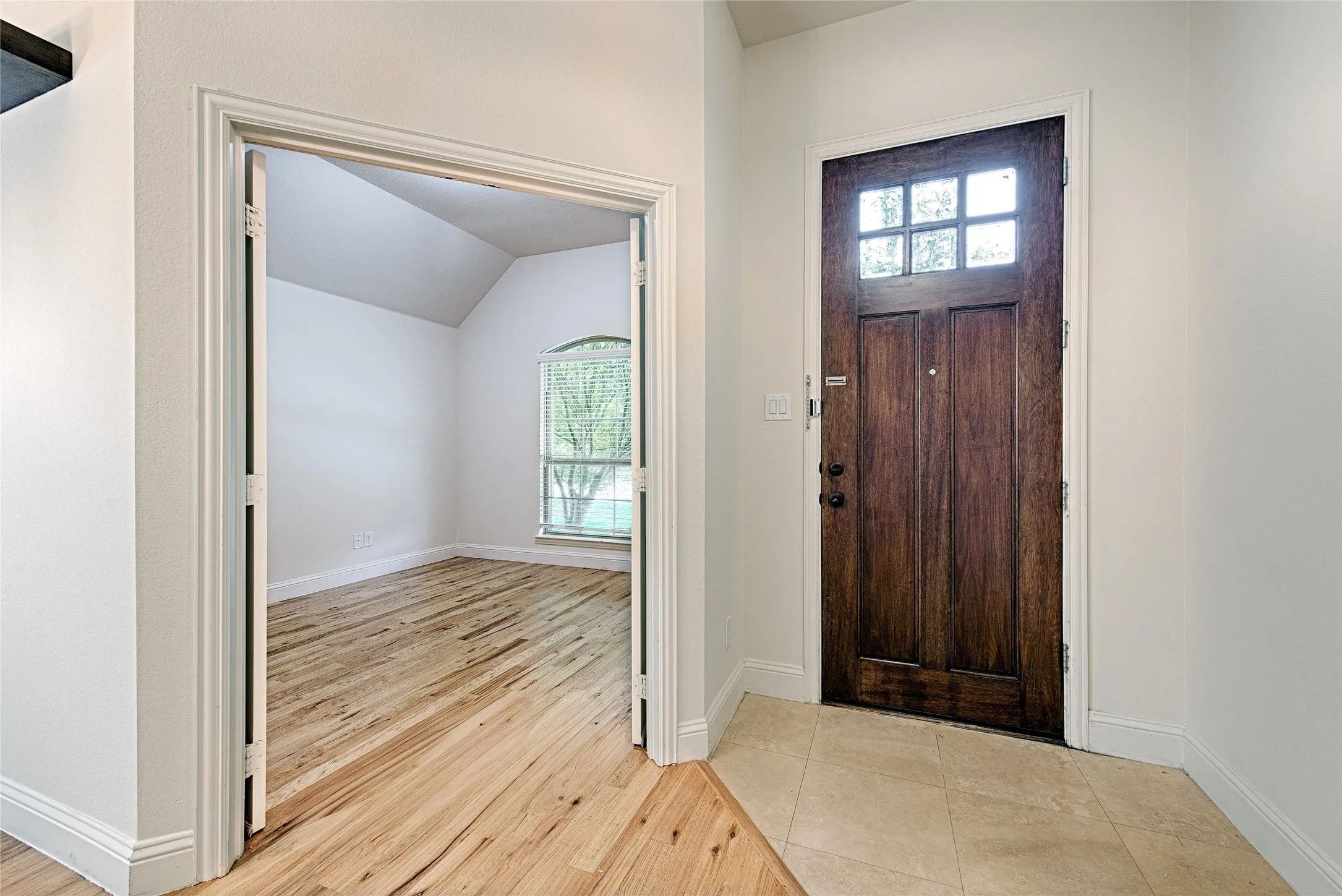 Entryway featuring a rich wood-paneled door with upper glass panes, neutral tile flooring, and crisp white walls