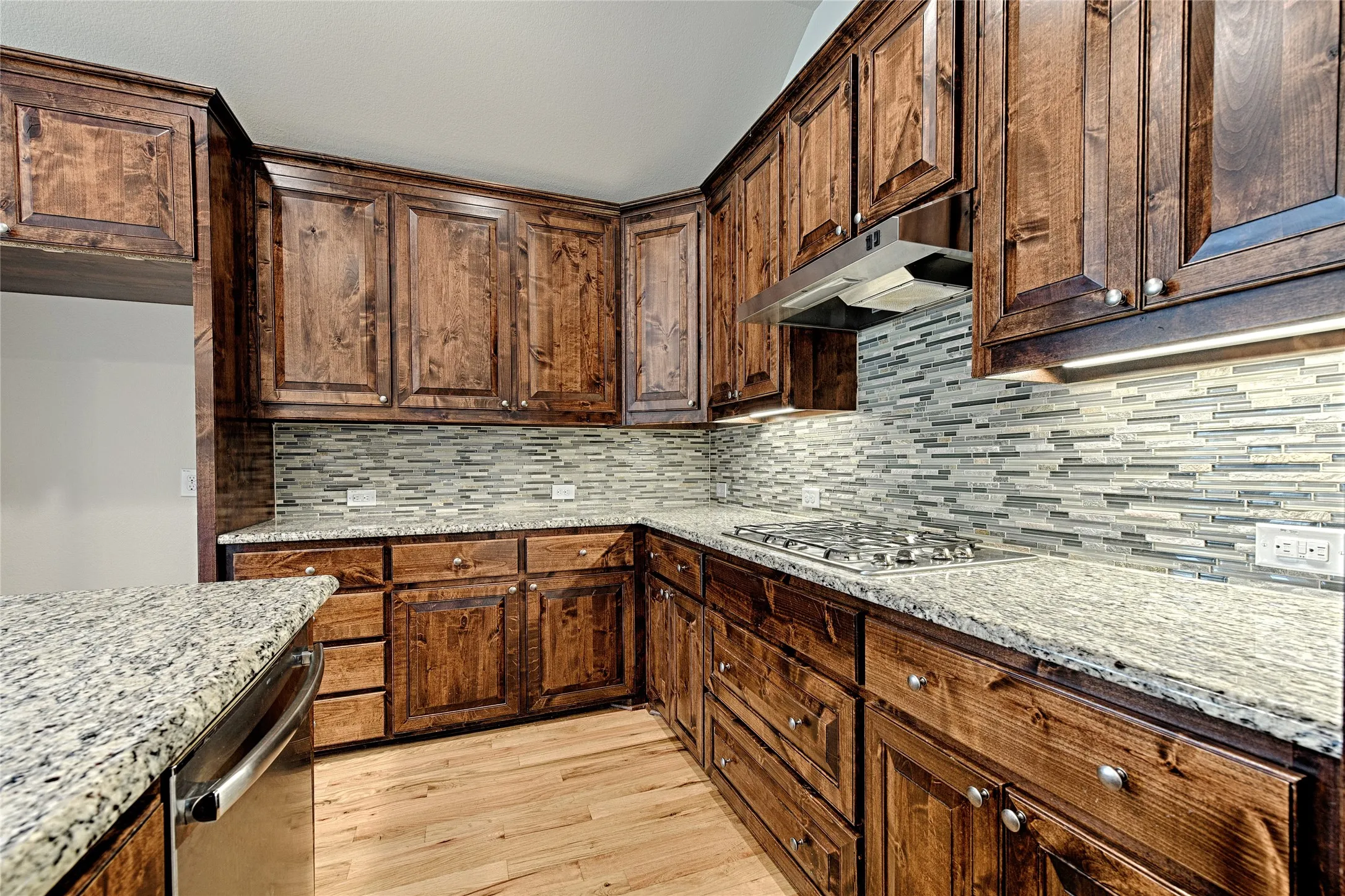 Kitchen featuring wood cabinetry, granite countertops, tile backsplash, built-in gas range, and wood-finish flooring