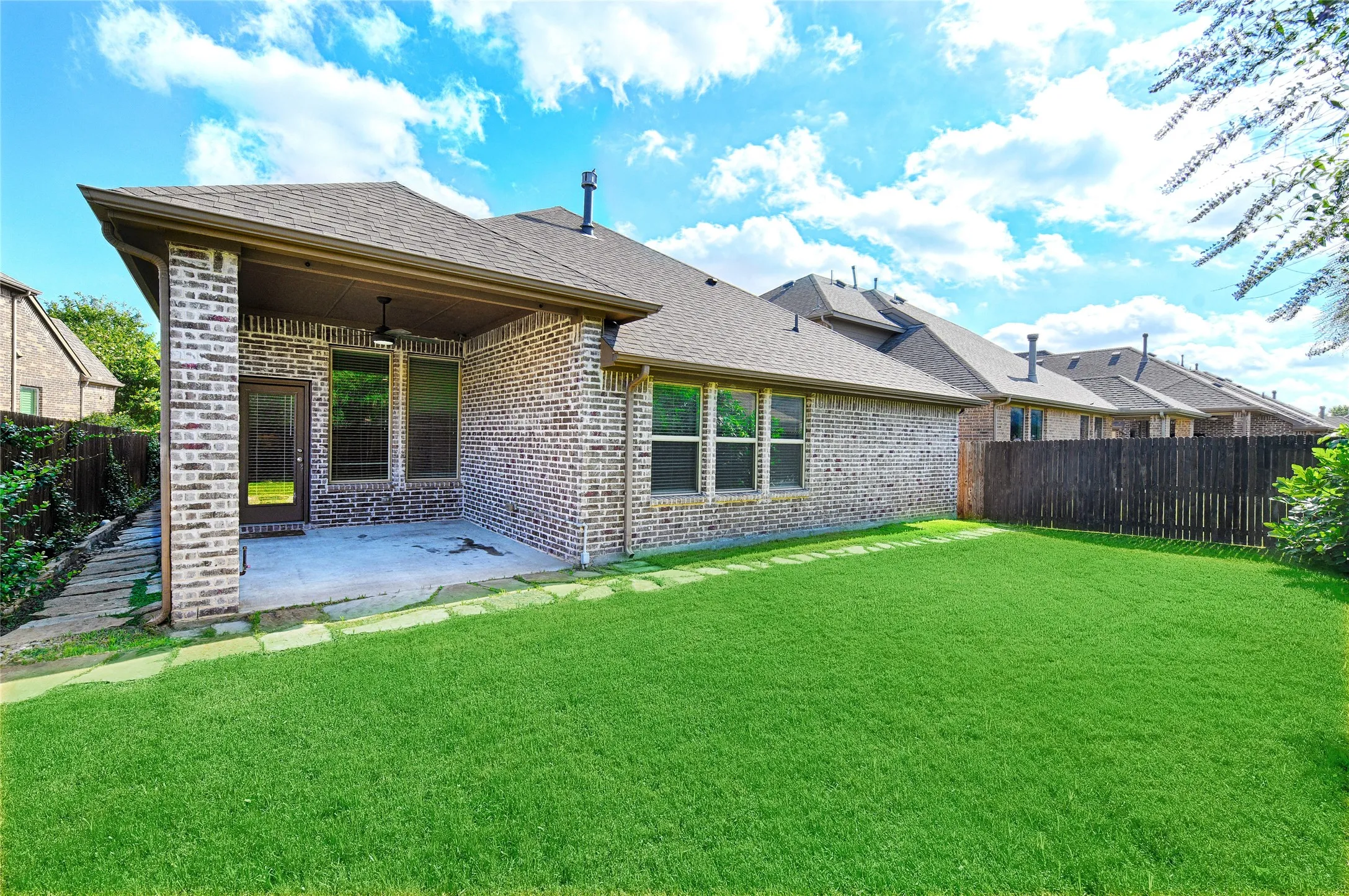 Expansive green lawn with a covered patio featuring a ceiling fan and brick columns