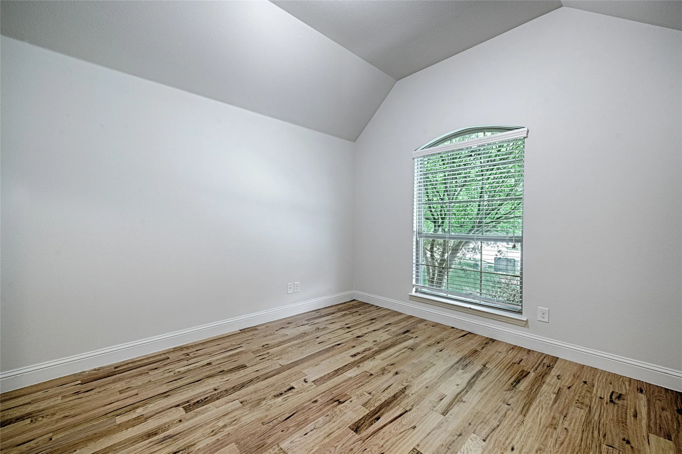 Room featuring vaulted ceilings, wood-finish flooring, and crisp white baseboards