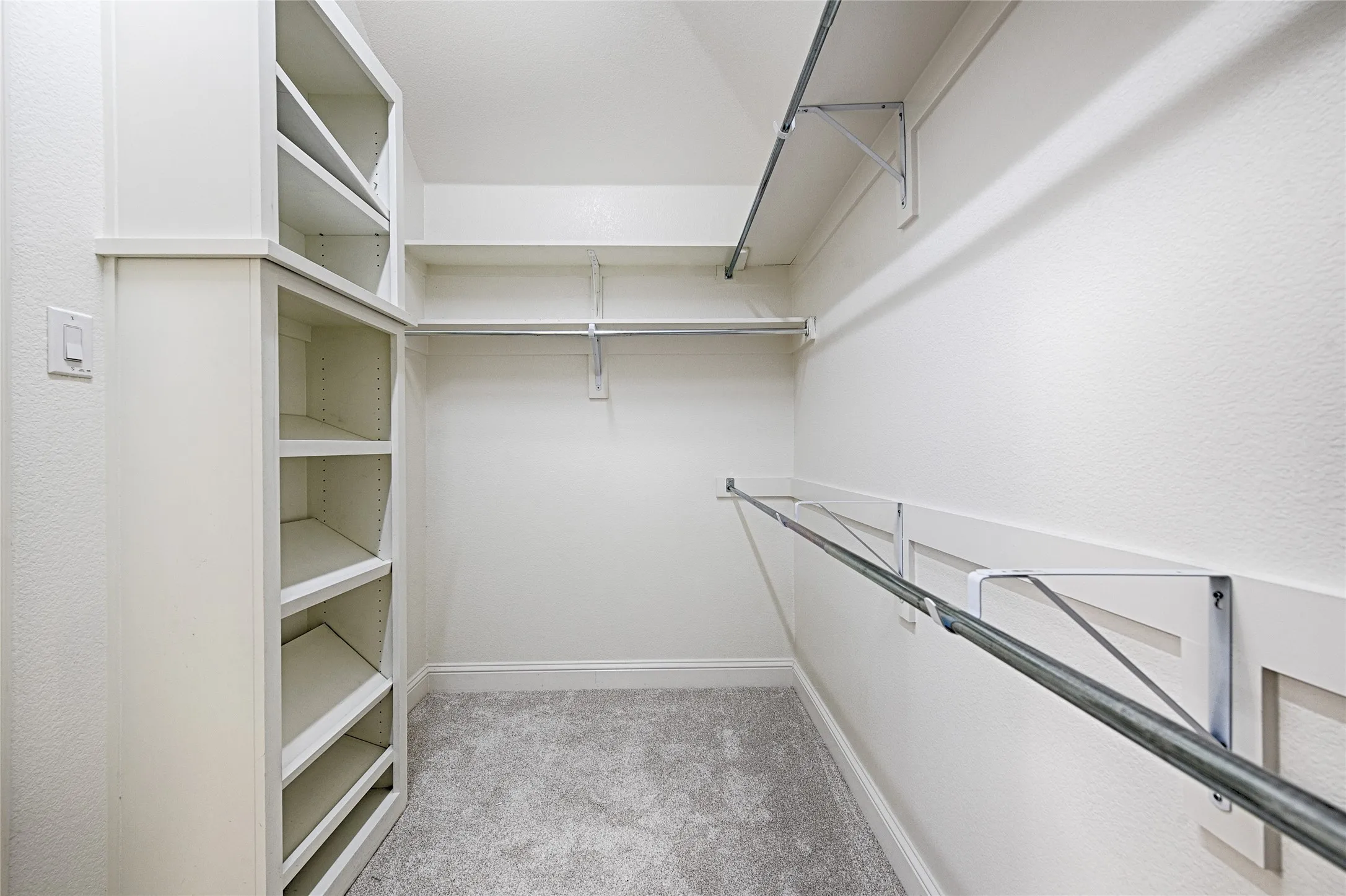 Walk-in closet featuring built-in shelving, multiple hanging rods, white textured walls, baseboards, and grey carpet flooring