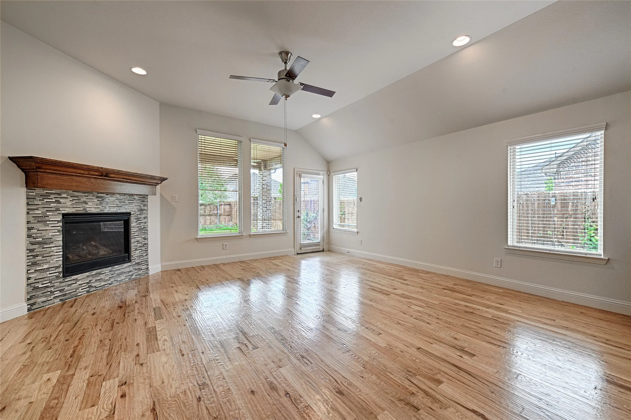 Spacious room featuring vaulted ceilings, recessed lighting, wood-finish flooring, and a fireplace with a stone-tile surround and wood mantel