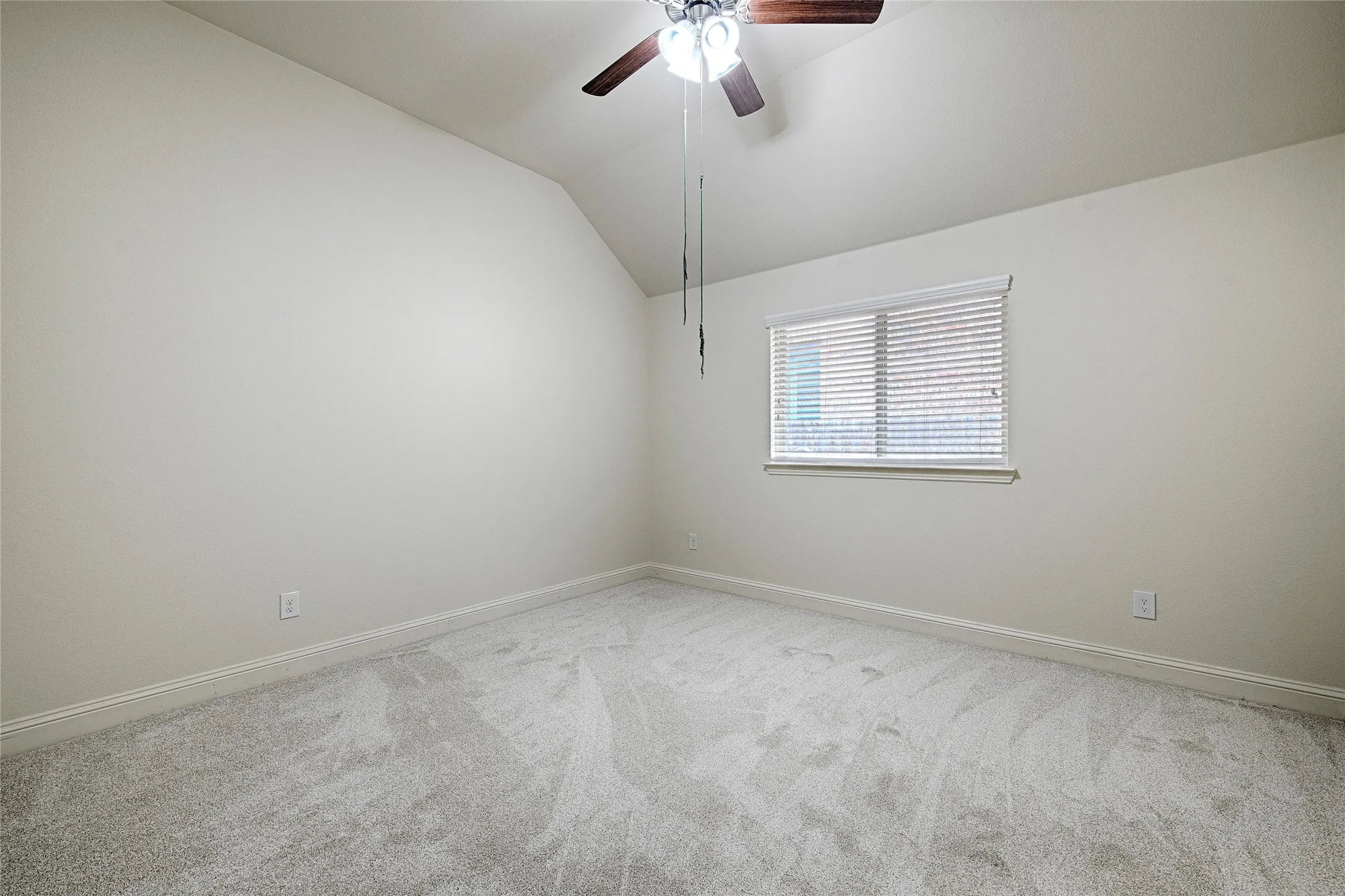 Room featuring an angled ceiling, light gray carpet, and a window with blinds