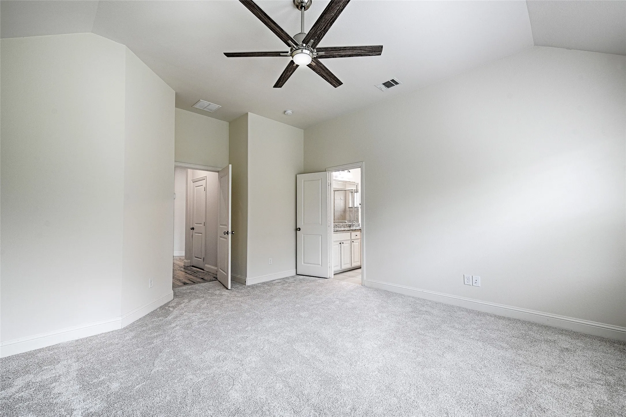 Spacious room featuring vaulted ceilings, light gray carpeting, and a dark wood-finish ceiling fan with integrated lighting