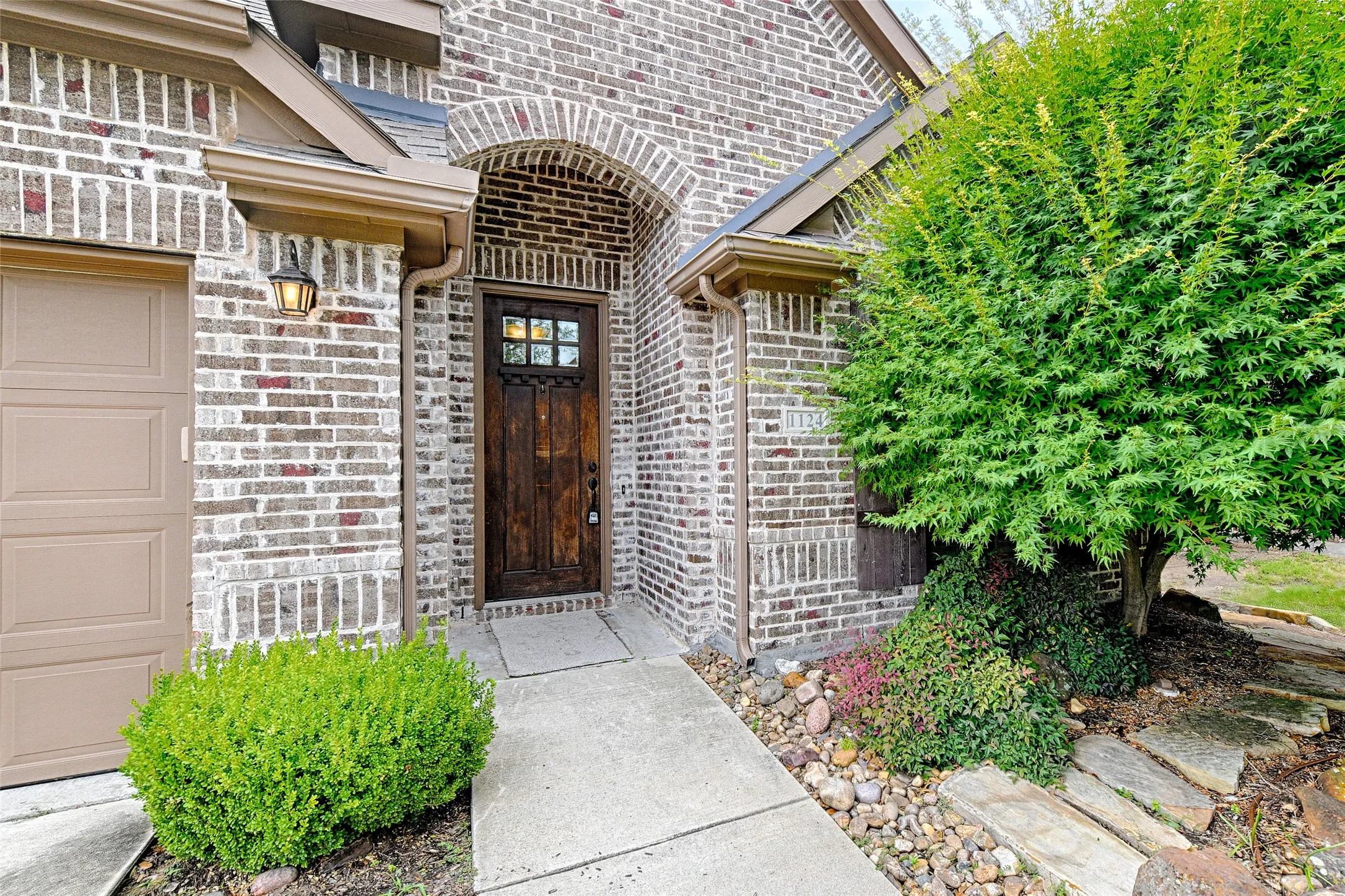 Brick facade entry featuring an arched doorway with a stained wood door