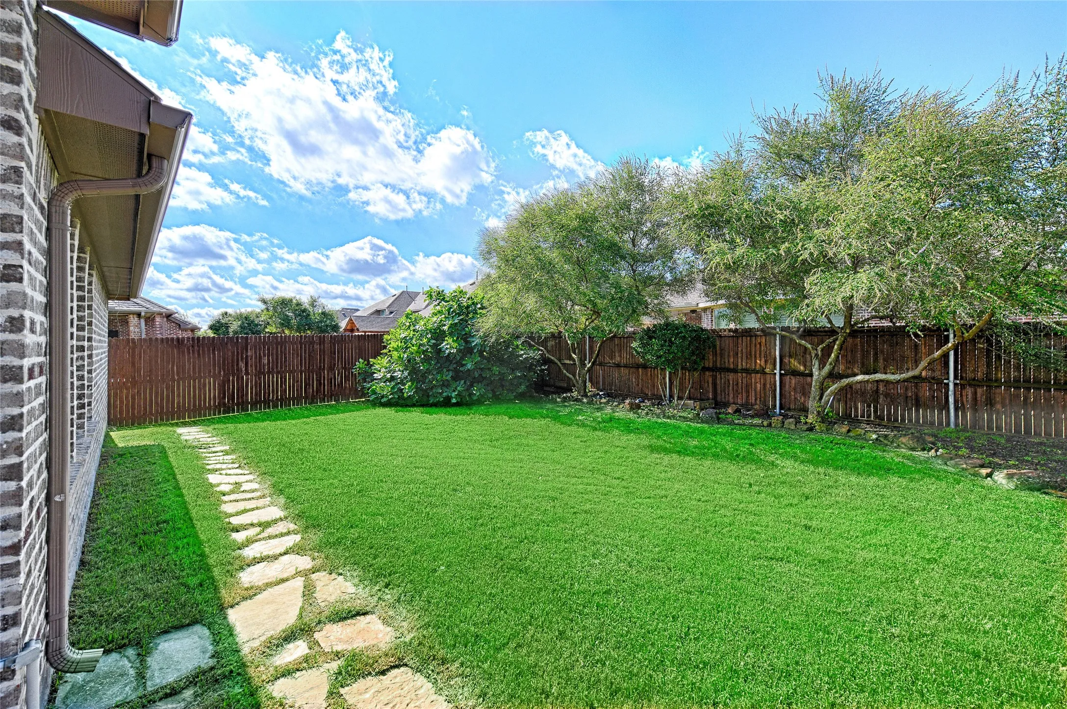 Expansive green lawn framed by a wooden privacy fence and mature trees