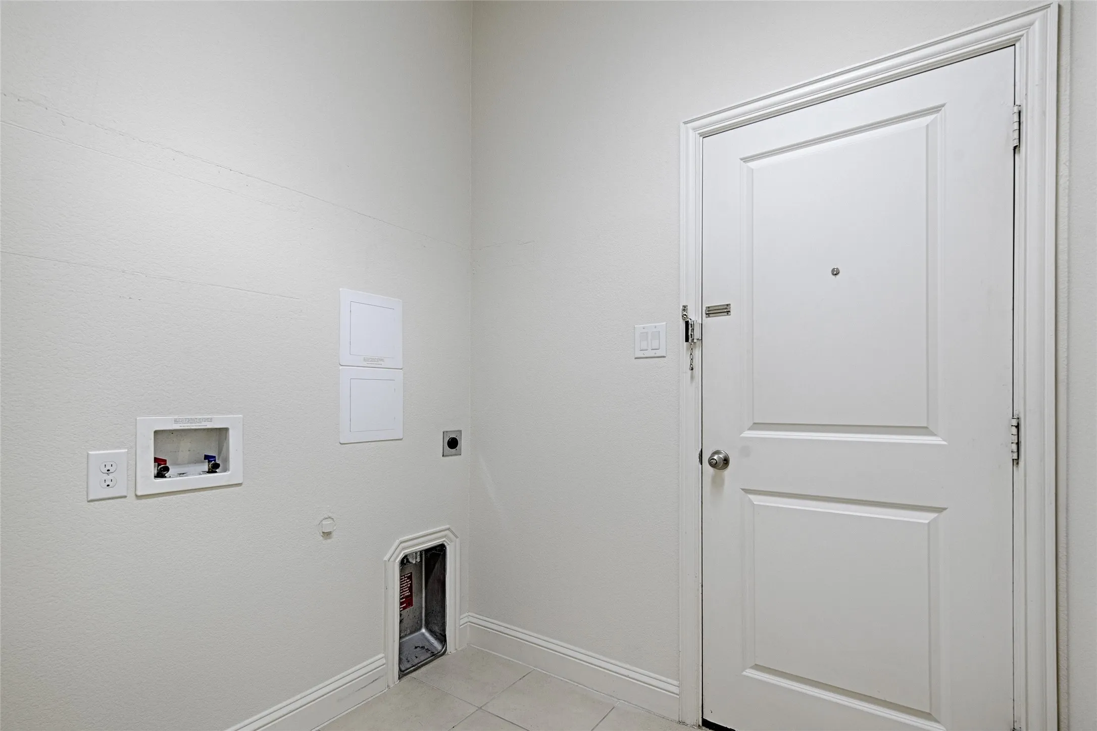 Dedicated utility area featuring tile flooring, white baseboards, and a paneled door with hardware